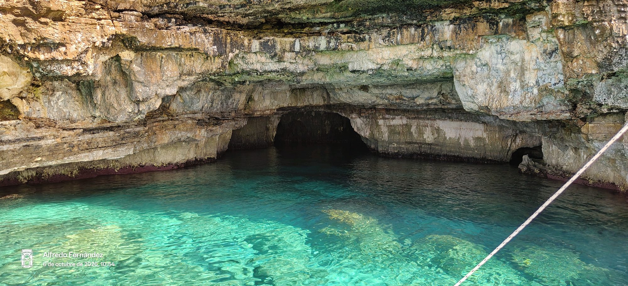 Cueva marina con aguas cristalinas de color turquesa bajo acantilados rocosos escarpados.