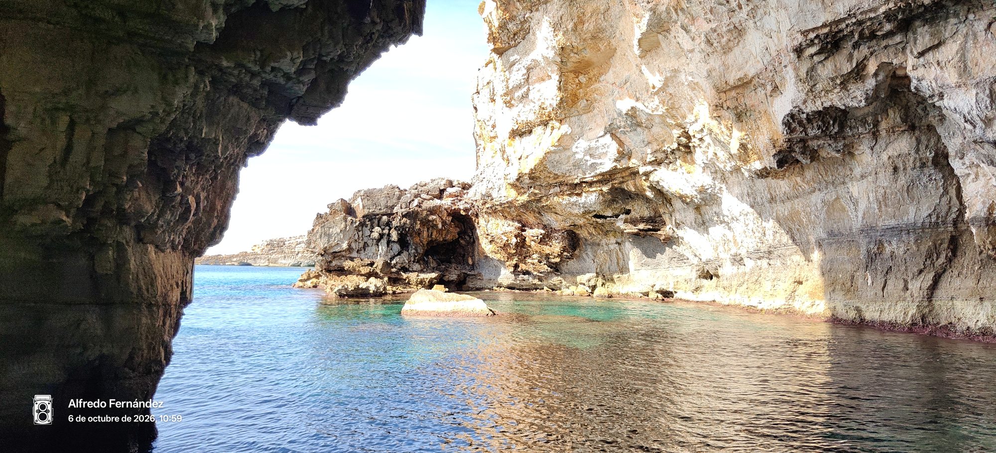 Vista desde el interior de una cueva marina hacia aguas turquesas y acantilados rocosos.
