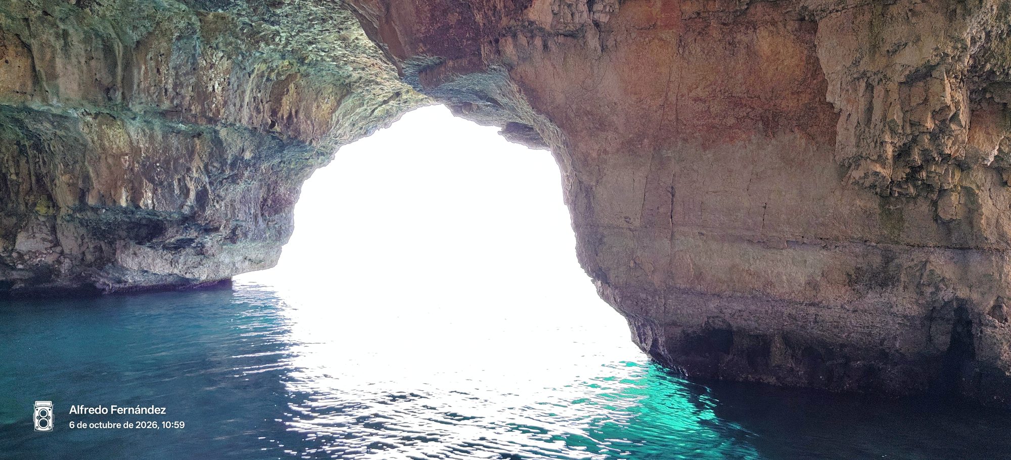 Interior de una cueva marina de roca caliza con agua turquesa cristalina.