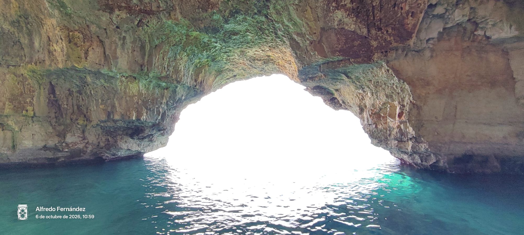Interior de una cueva marina con aguas turquesas iluminadas por la luz del exterior.