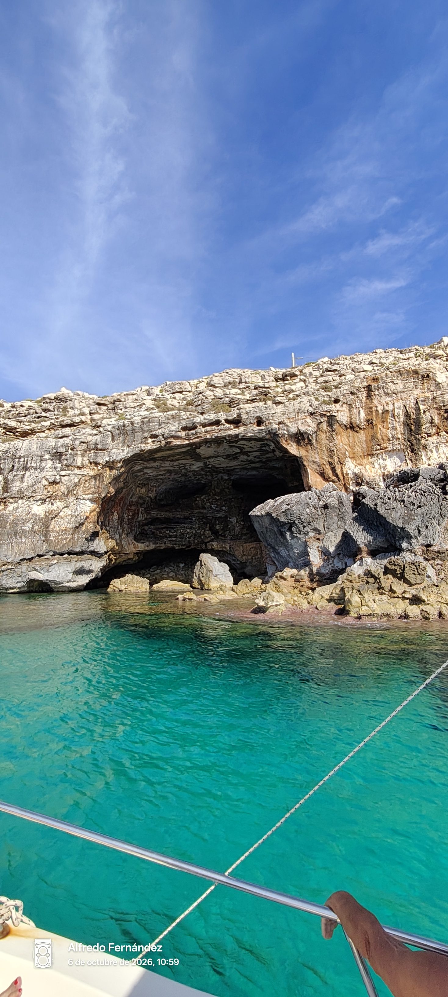 Cueva marina en acantilados rocosos frente a aguas turquesas cristalinas bajo cielo azul.