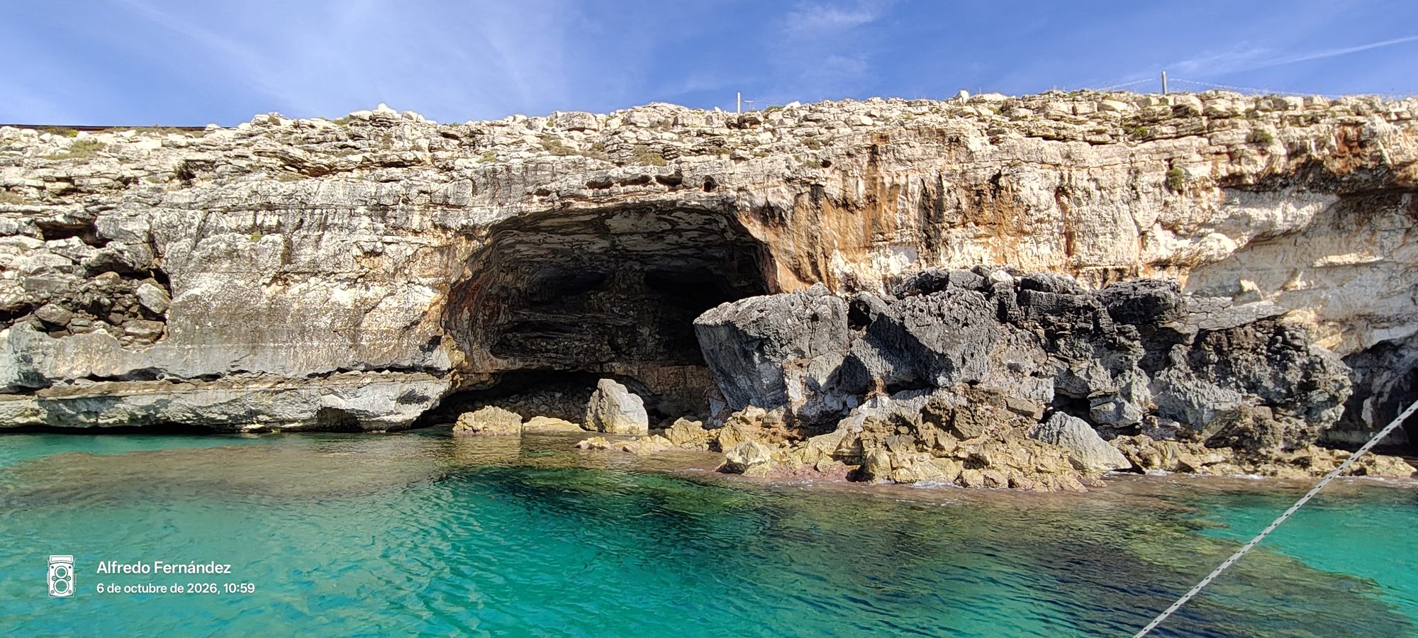 Cueva marina natural tallada en acantilados rocosos junto a aguas cristalinas de color turquesa.