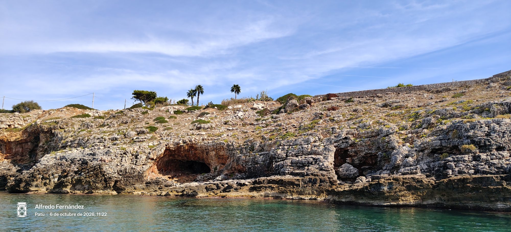 Acantilados rocosos con cuevas marinas junto al mar turquesa bajo un cielo despejado.