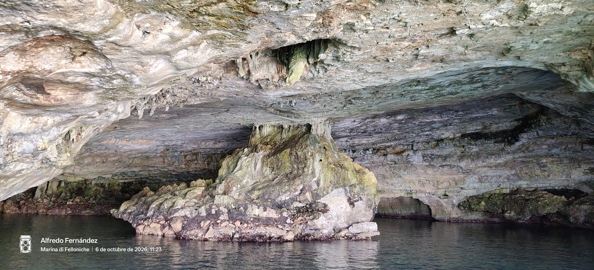 Interior de una cueva marina de roca caliza con aguas tranquilas y columnas naturales.