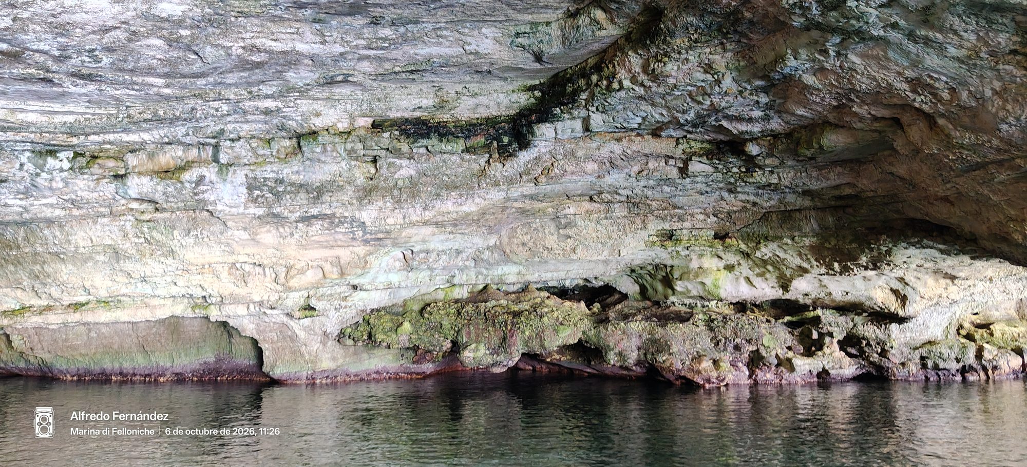 Cueva marina con formaciones rocosas estratificadas sobre aguas cristalinas y tranquilas.