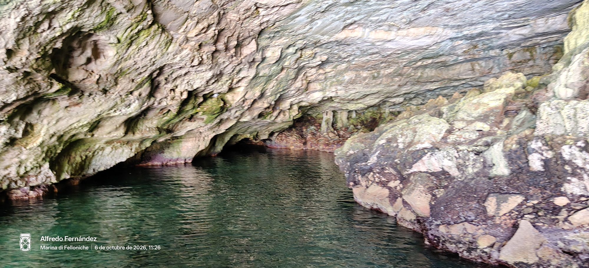 Interior de una cueva marina con paredes rocosas y aguas verdes transparentes.