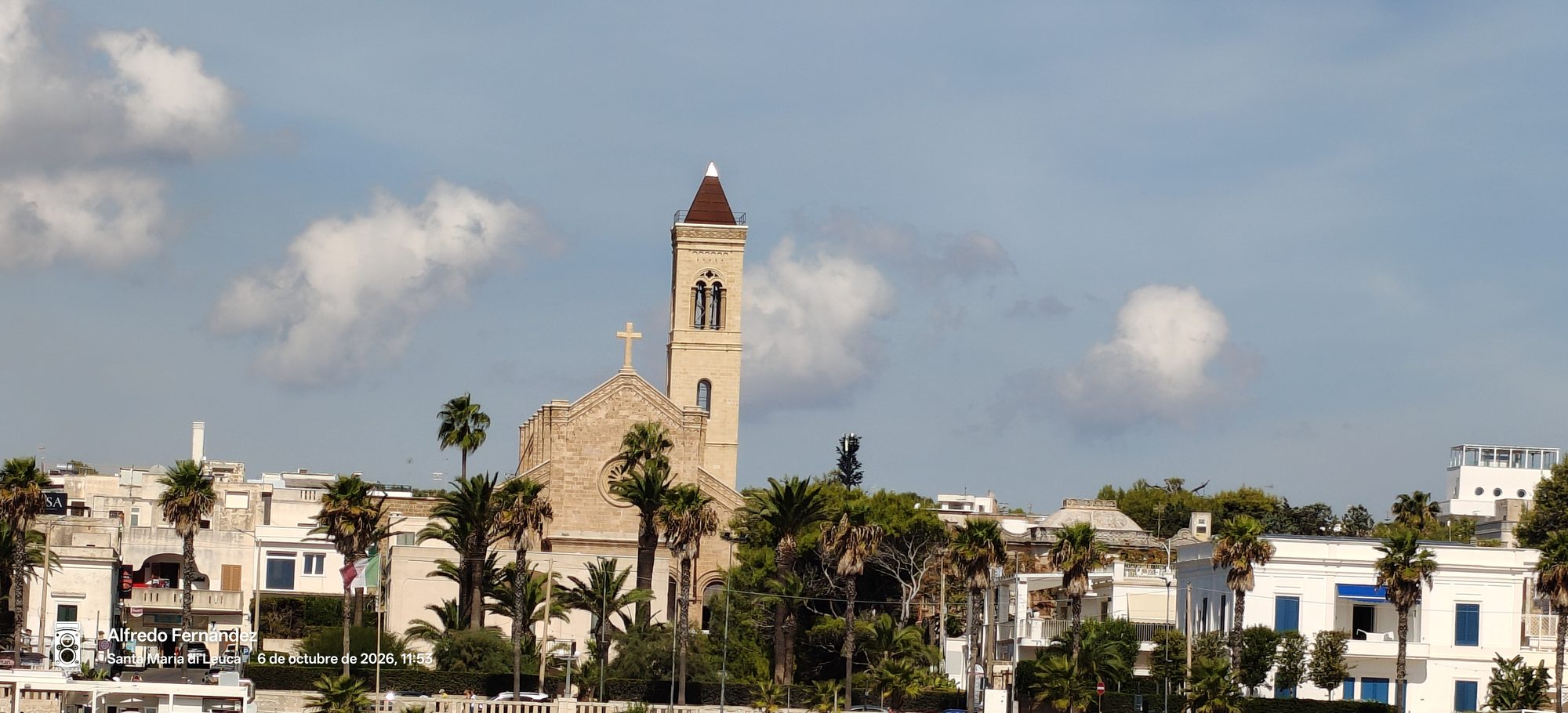 Iglesia de piedra con campanario rodeada de palmeras bajo un cielo despejado.
