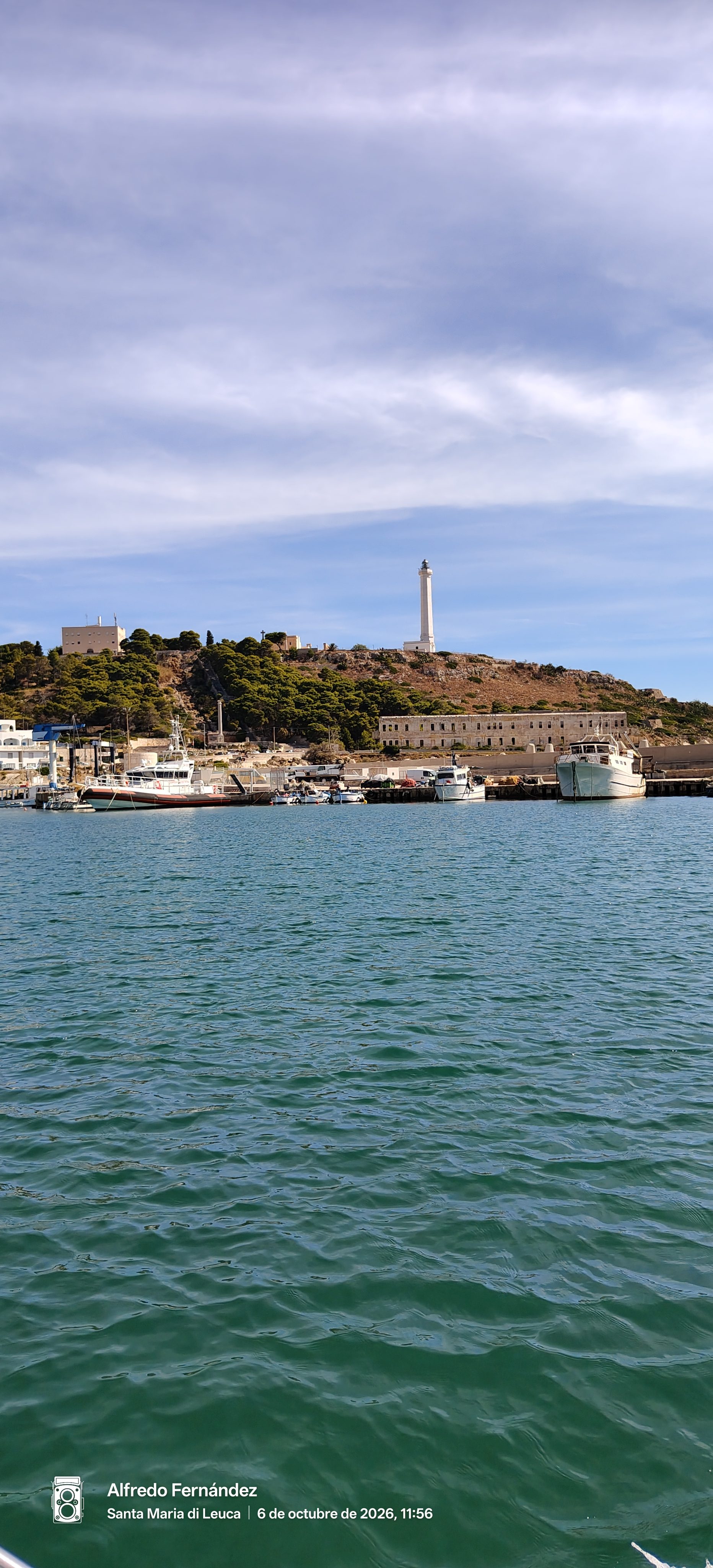 Puerto de Santa Maria di Leuca con barcos amarrados y faro blanco en la colina.