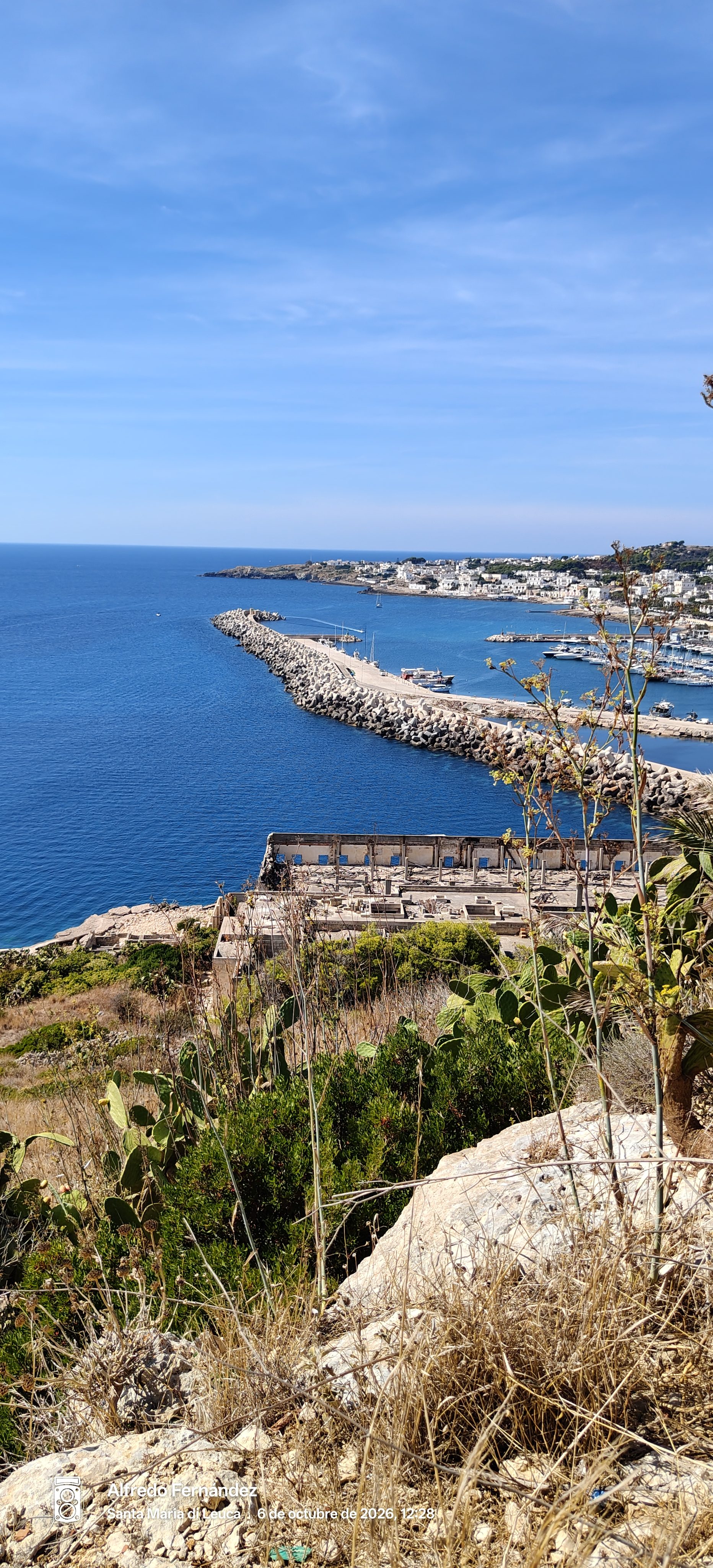 Vista elevada del puerto y espigón marítimo frente al mar azul en la costa.