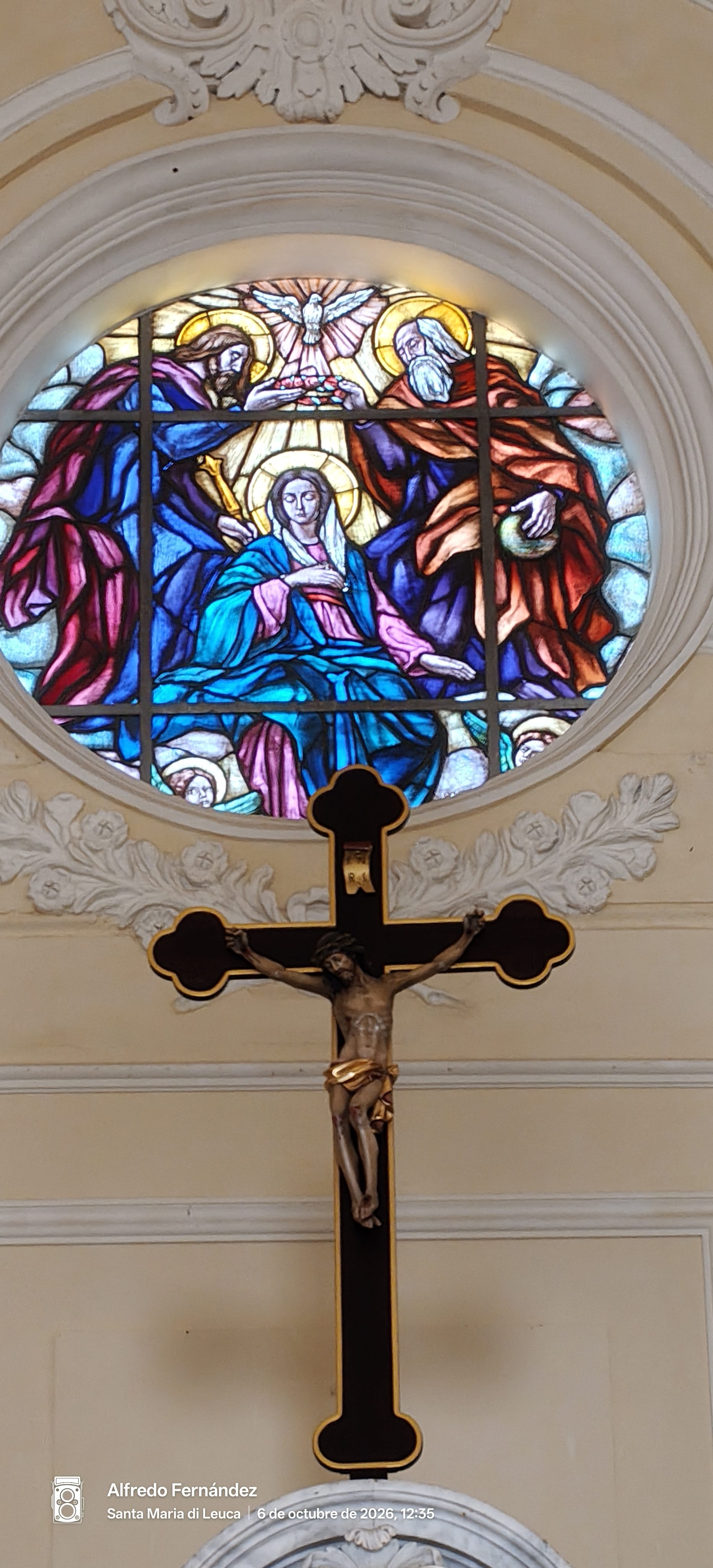 Crucifijo tallado bajo una colorida vidriera religiosa en el interior de una iglesia.