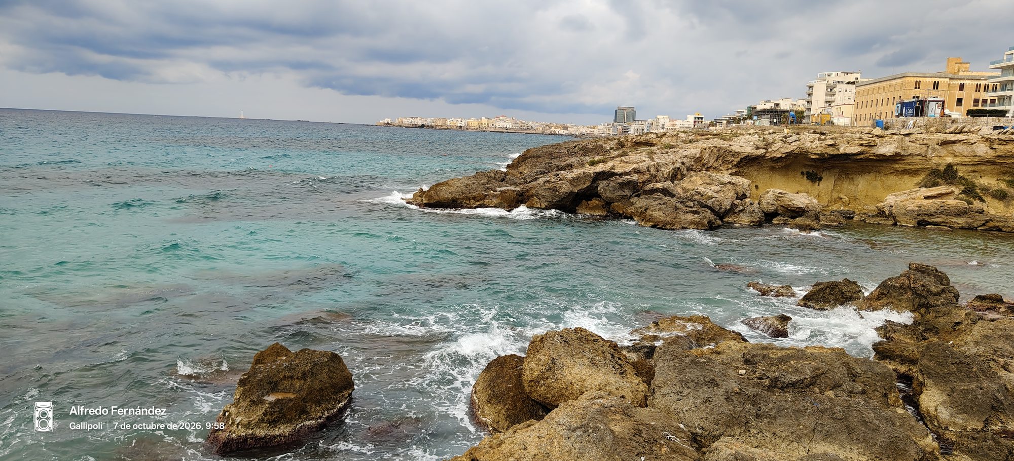 Costa rocosa con mar turquesa frente a los acantilados y edificios costeros.