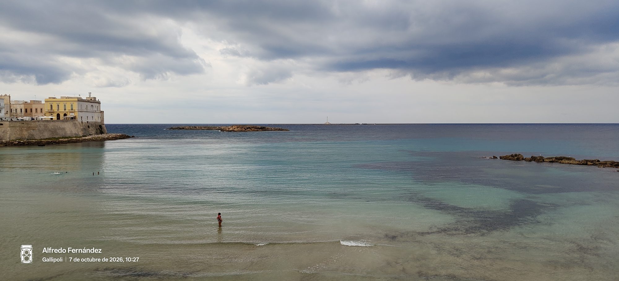 Costa de Gallipoli con aguas cristalinas turquesas, edificios históricos y cielo nublado.