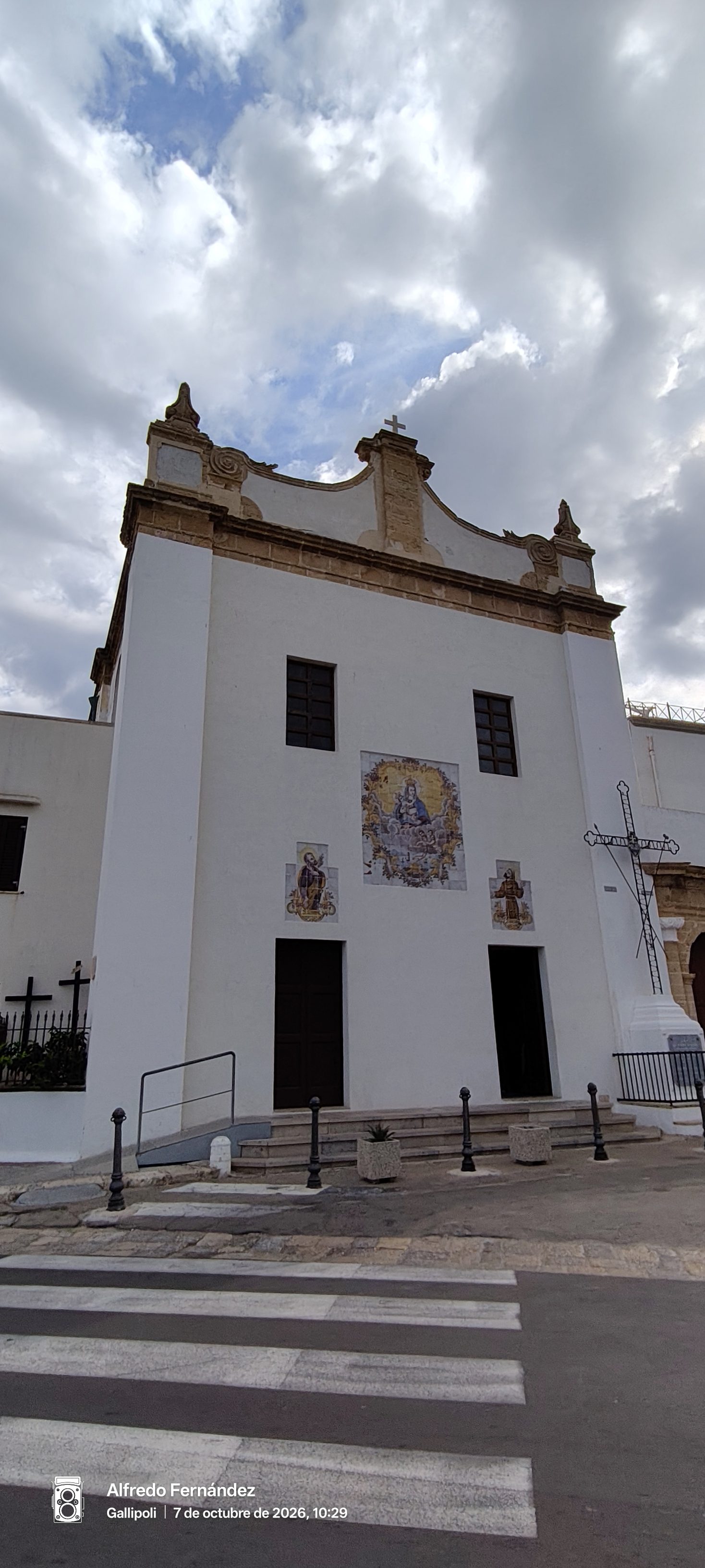 Fachada blanca de iglesia tradicional con mosaicos religiosos bajo un cielo nublado en Gallipoli.