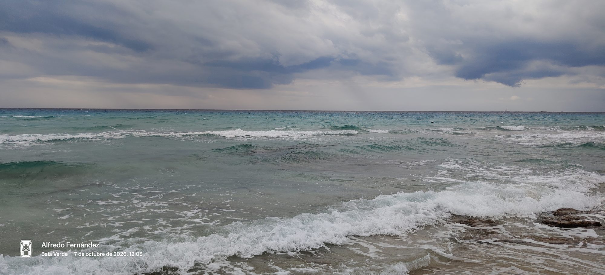 Olas del mar turquesa rompiendo bajo un cielo nublado y tormentoso en la playa.