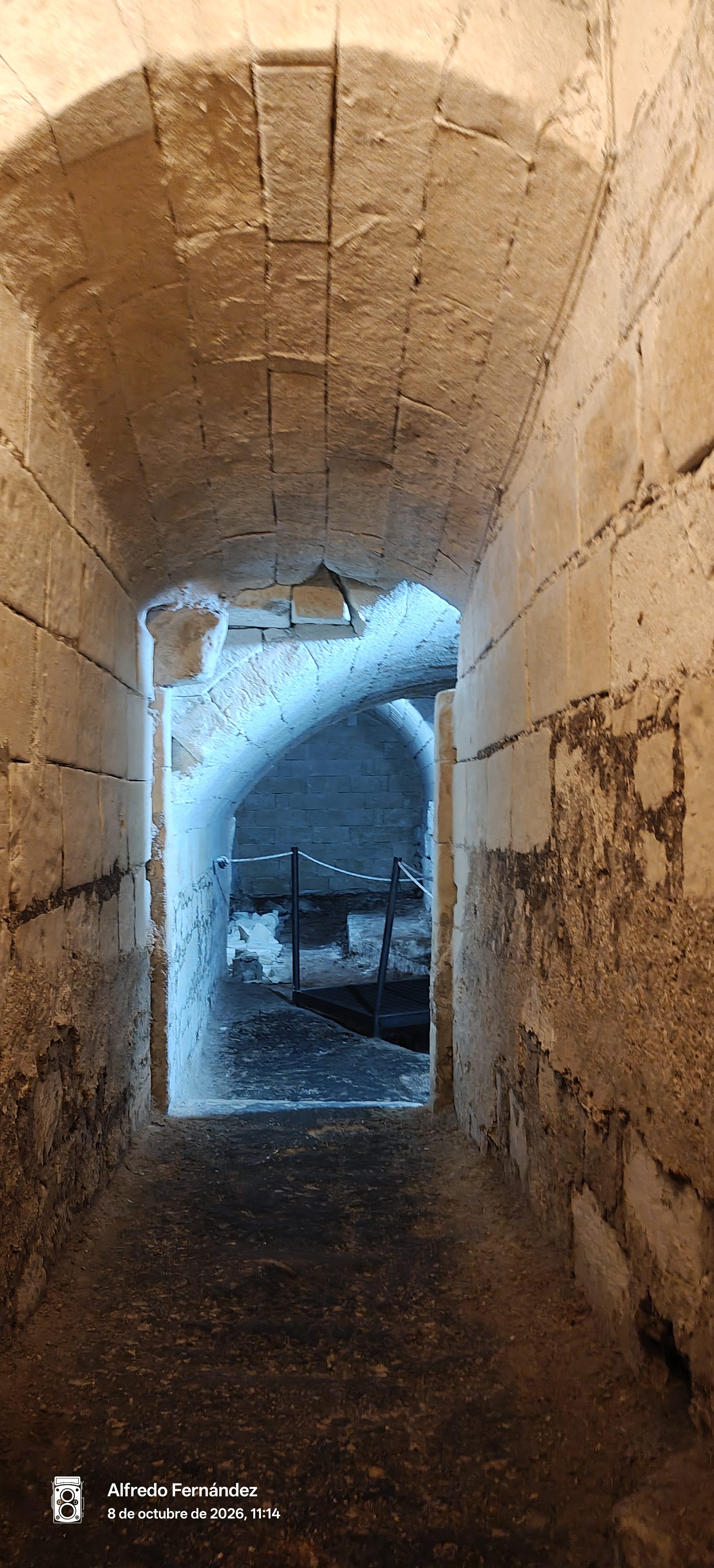 Pasadizo abovedado de piedra antigua que conduce a galerías subterráneas iluminadas.