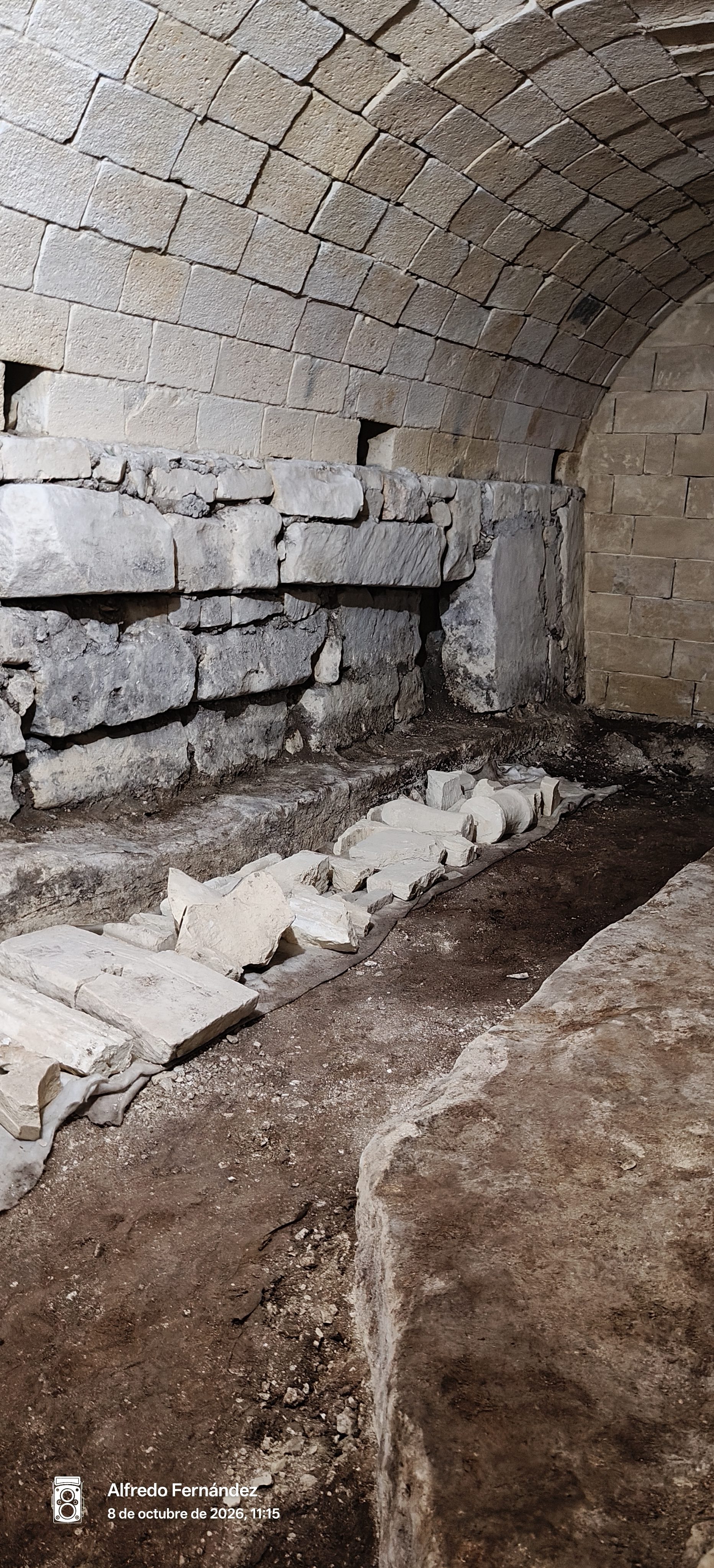 Bóveda de piedra antigua con restos arqueológicos y bloques tallados en el suelo.