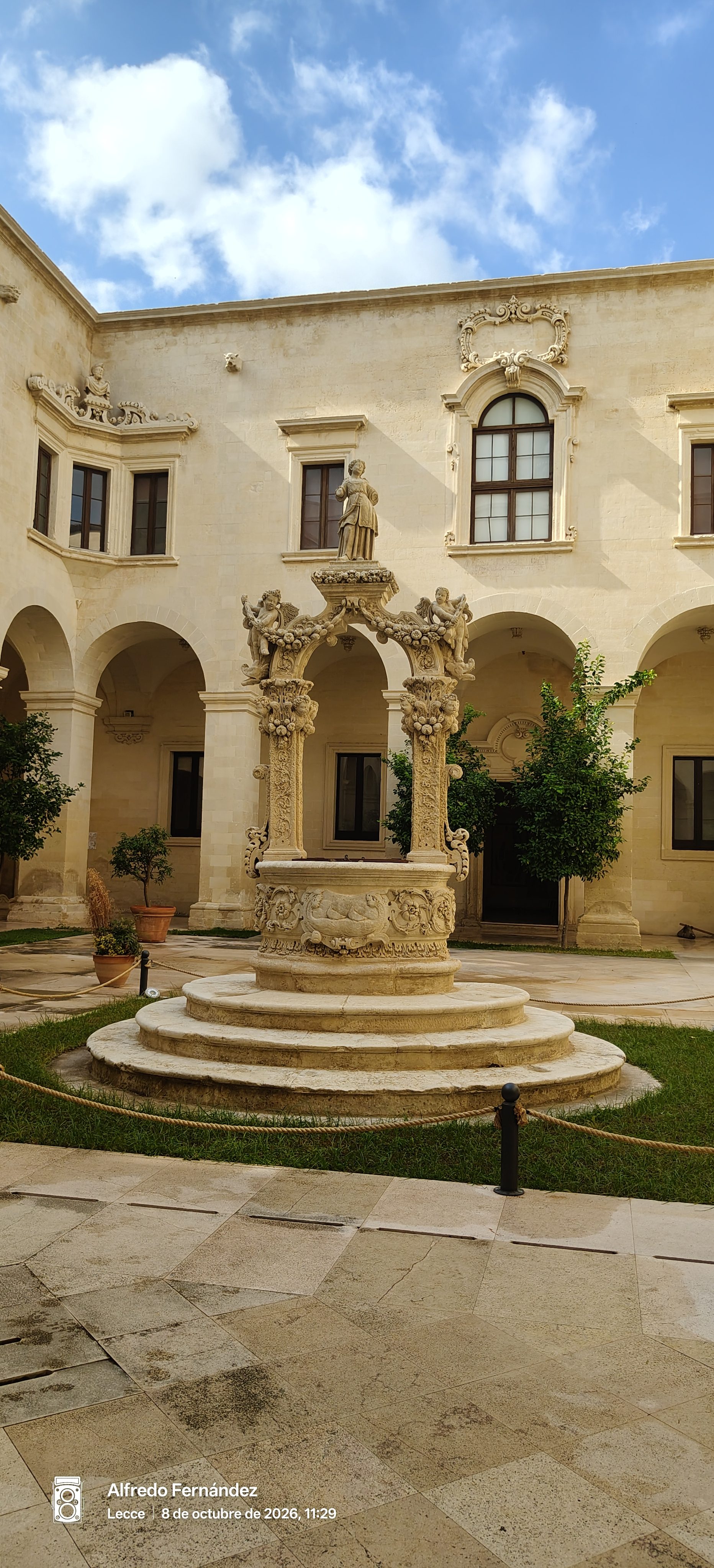 Pozo barroco de piedra caliza profusamente tallado en el patio de un claustro histórico.
