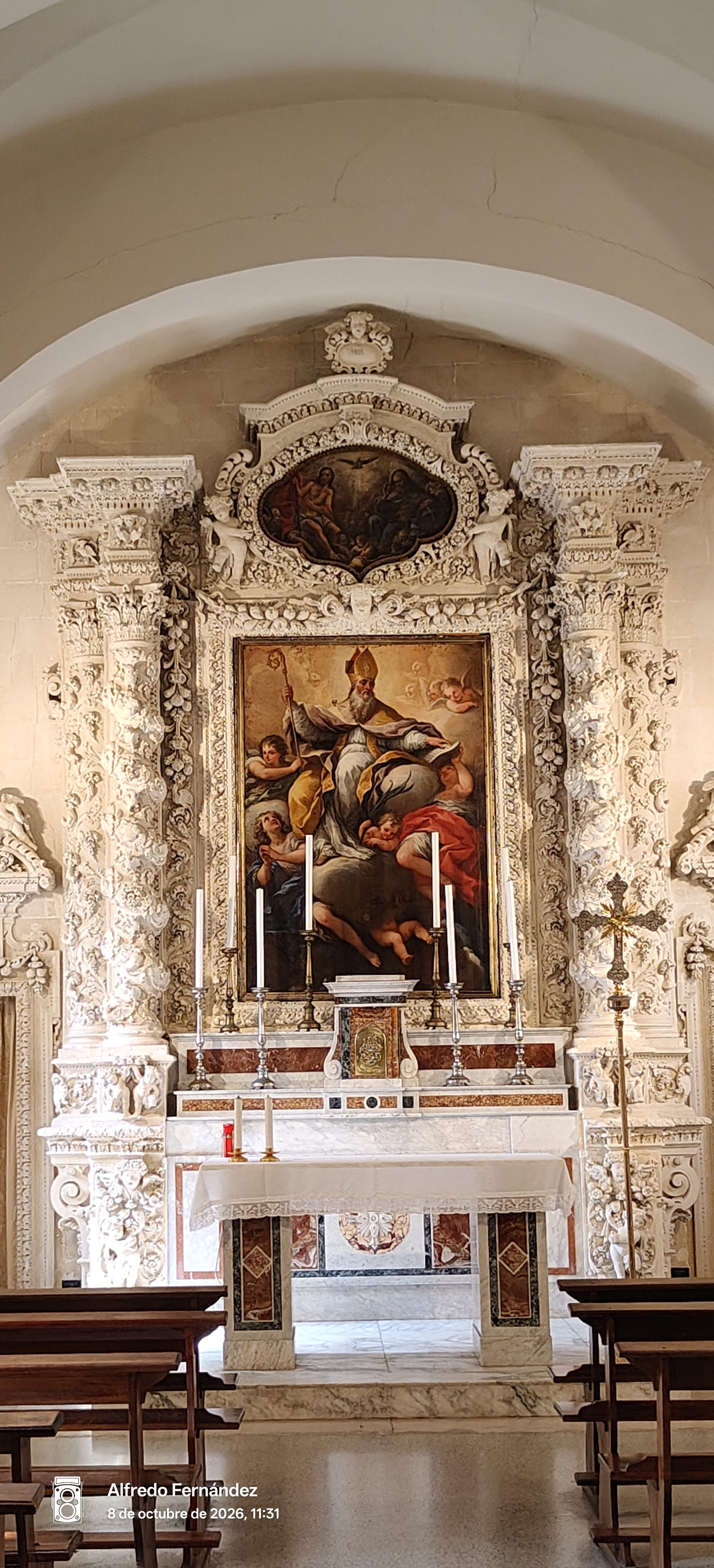 Altar barroco de piedra blanca tallada con pintura religiosa y candelabros en una iglesia.