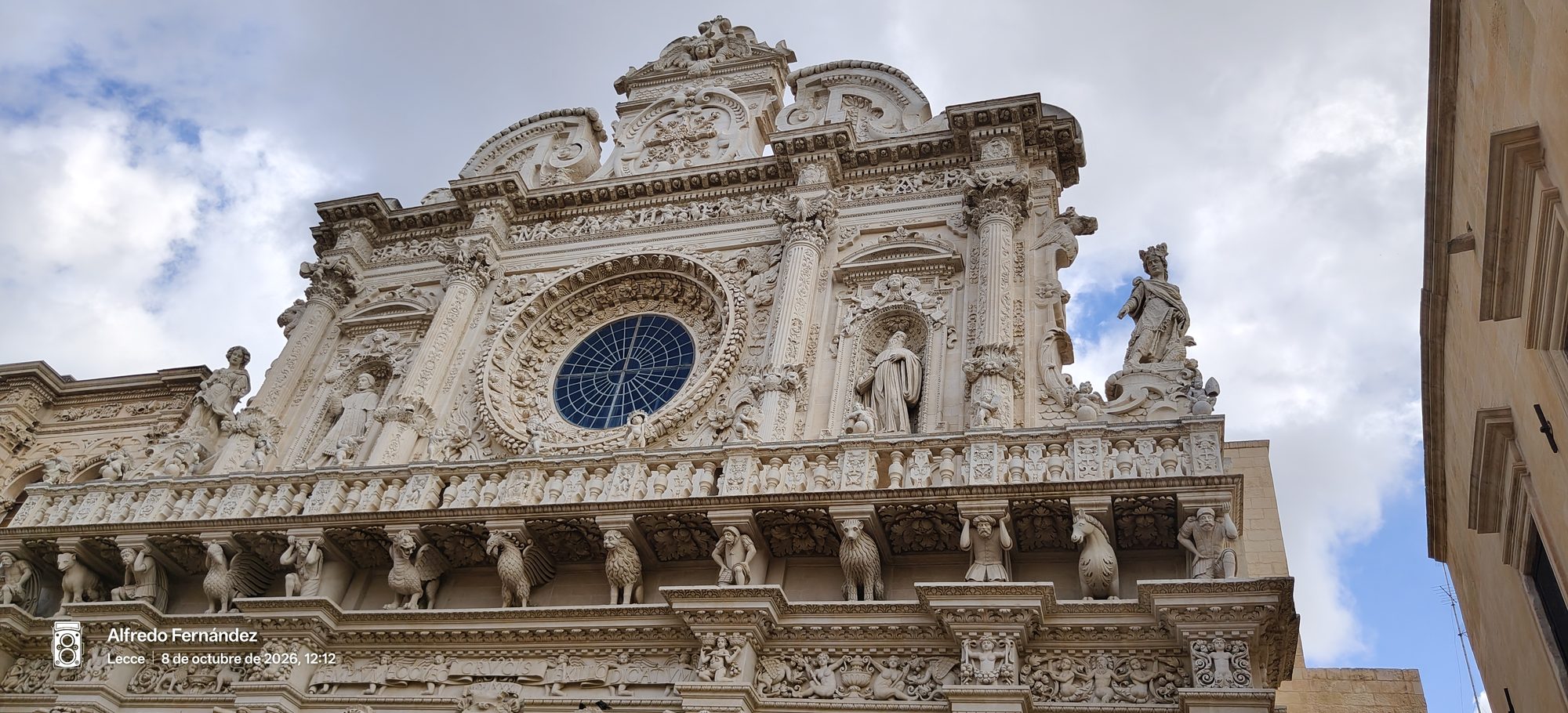 Detallada fachada barroca de piedra con rosetón y esculturas de la Basílica de Santa Cruz.
