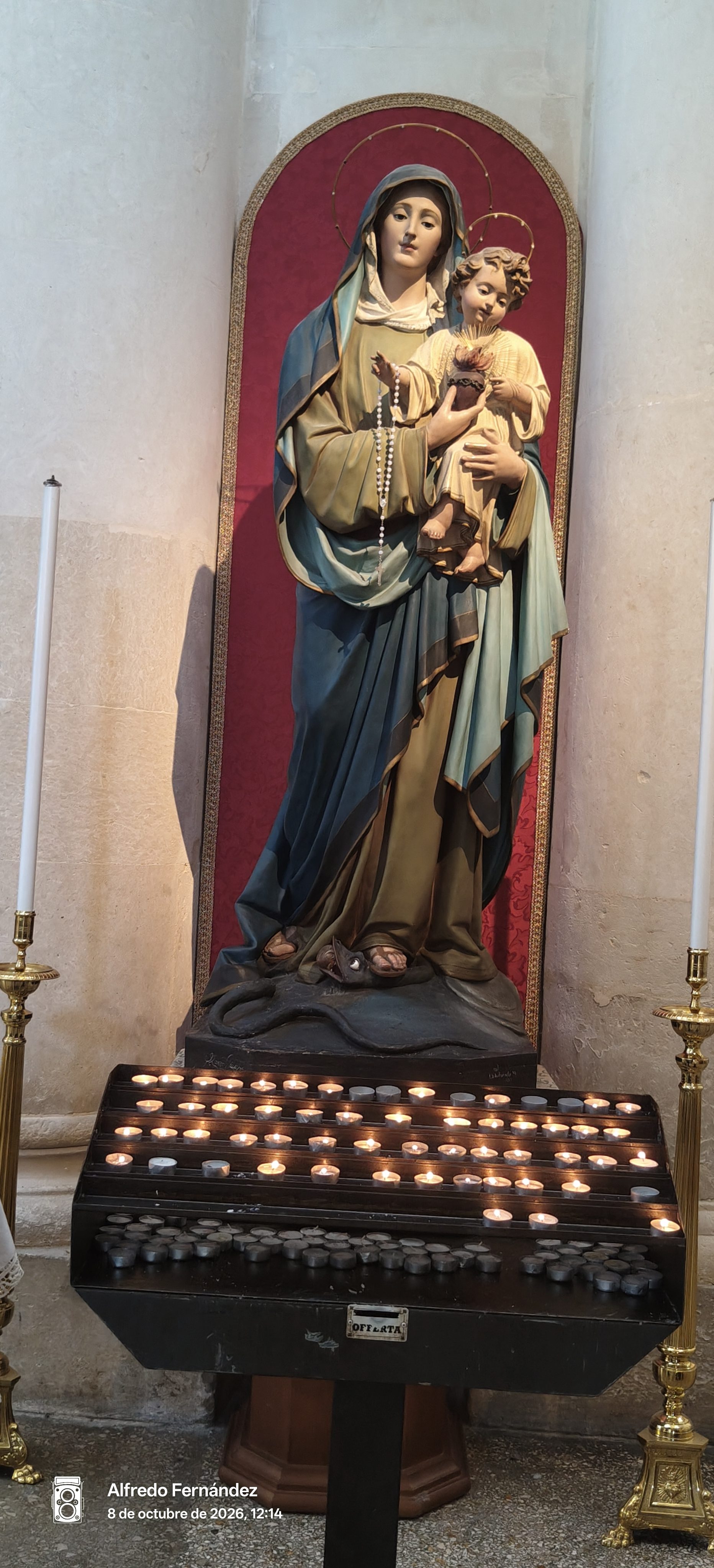 Estatua religiosa de la Virgen María con el Niño Jesús y velas devocionales encendidas.