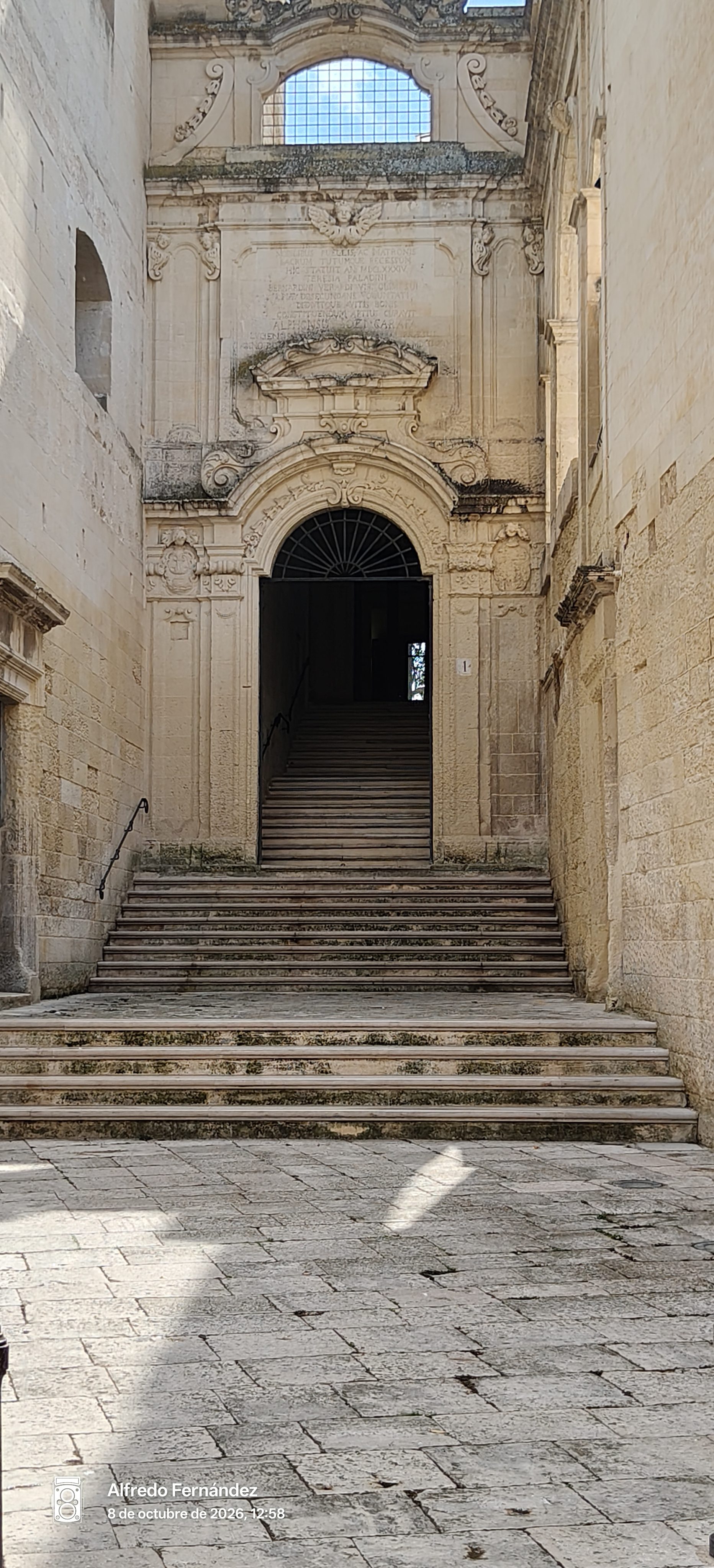 Escalinata de piedra que conduce a una portada barroca ornamentada con inscripciones antiguas.