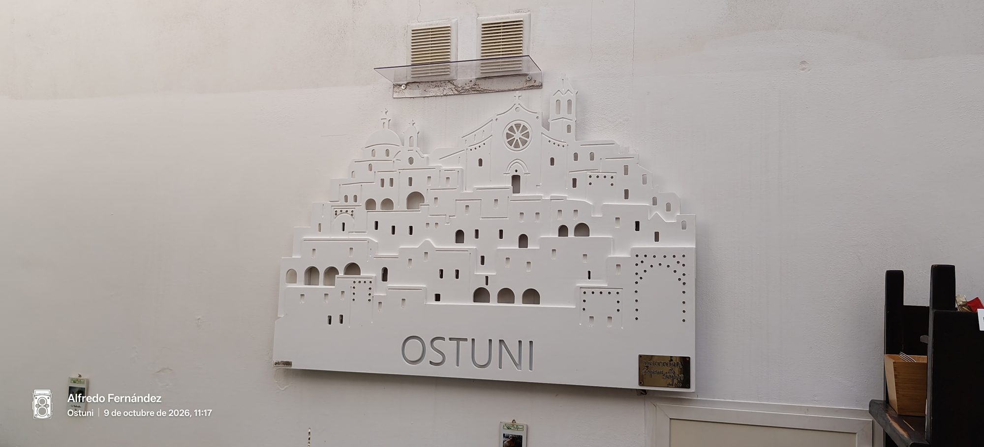 Relieve decorativo blanco en una pared que recrea la silueta urbana de Ostuni.