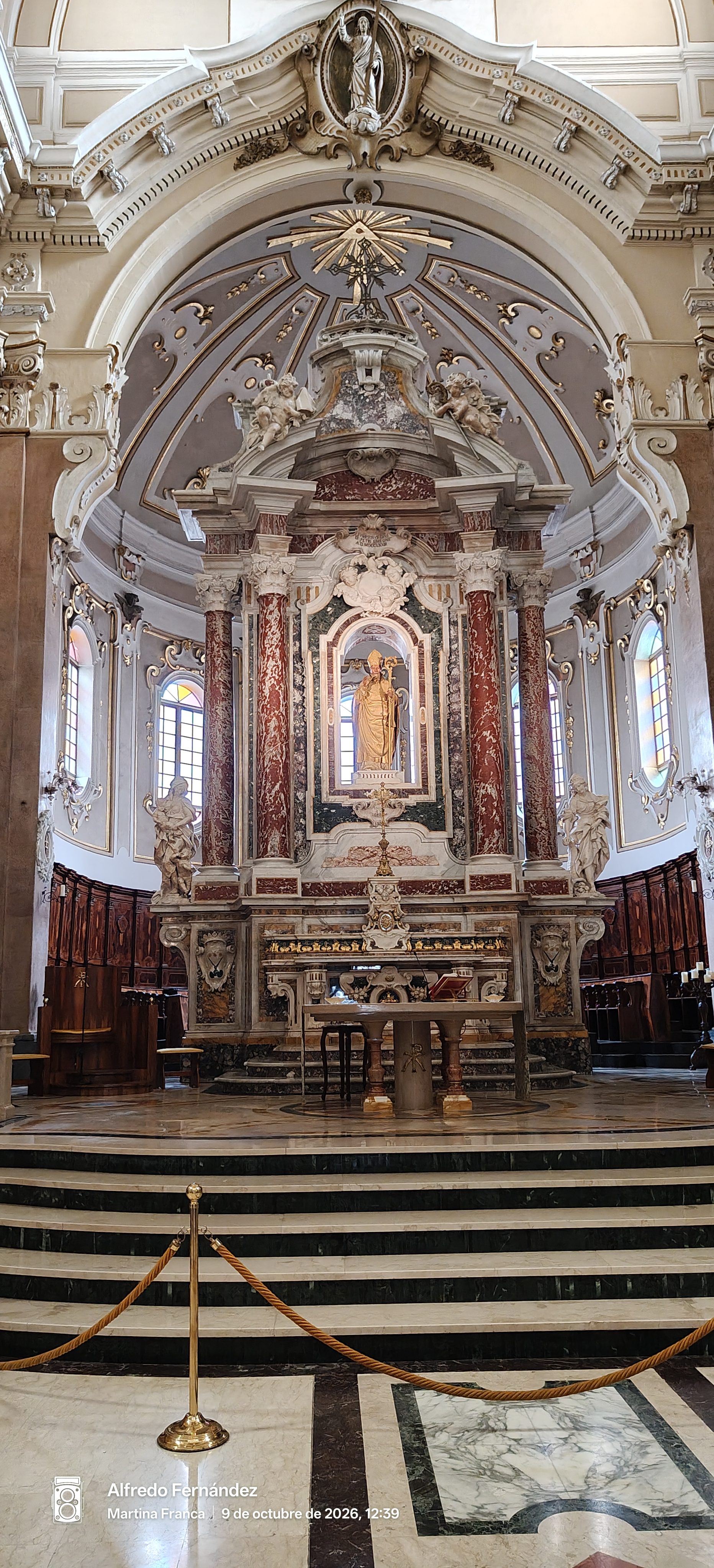 Altar mayor barroco con columnas de mármol rojizo y esculturas en una basílica italiana.