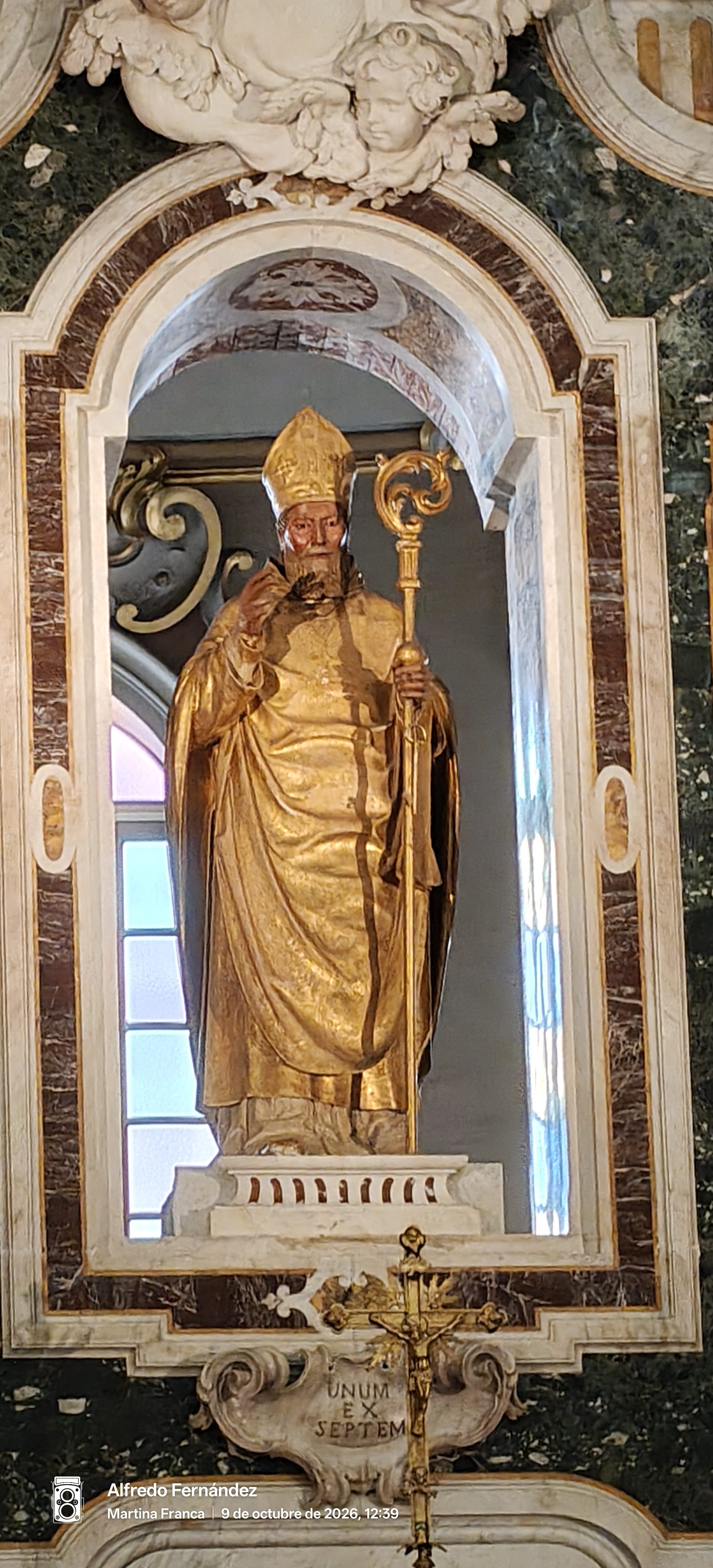 Estatua dorada de un obispo con báculo dentro de una hornacina de mármol.