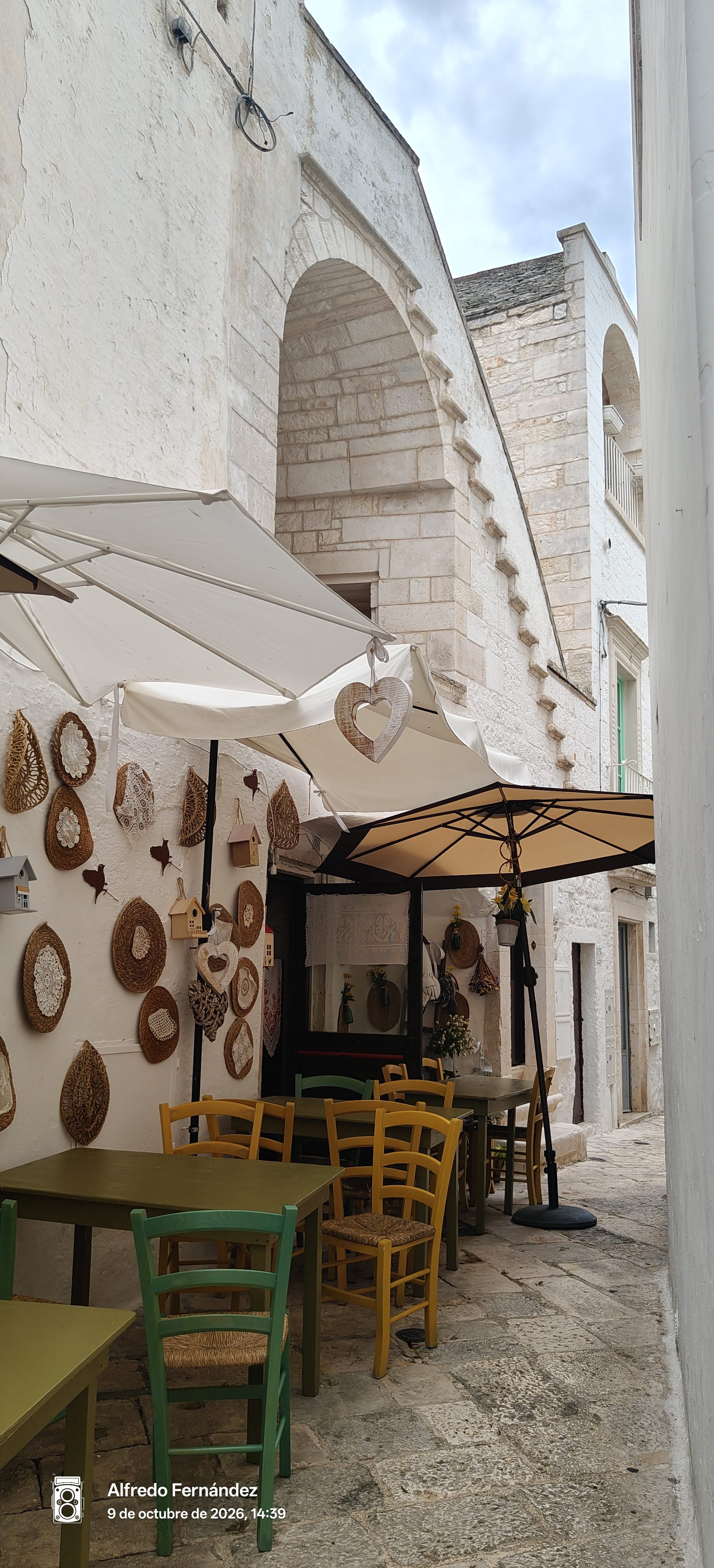 Callejón blanco con terraza de restaurante decorada con artesanías y sillas de colores