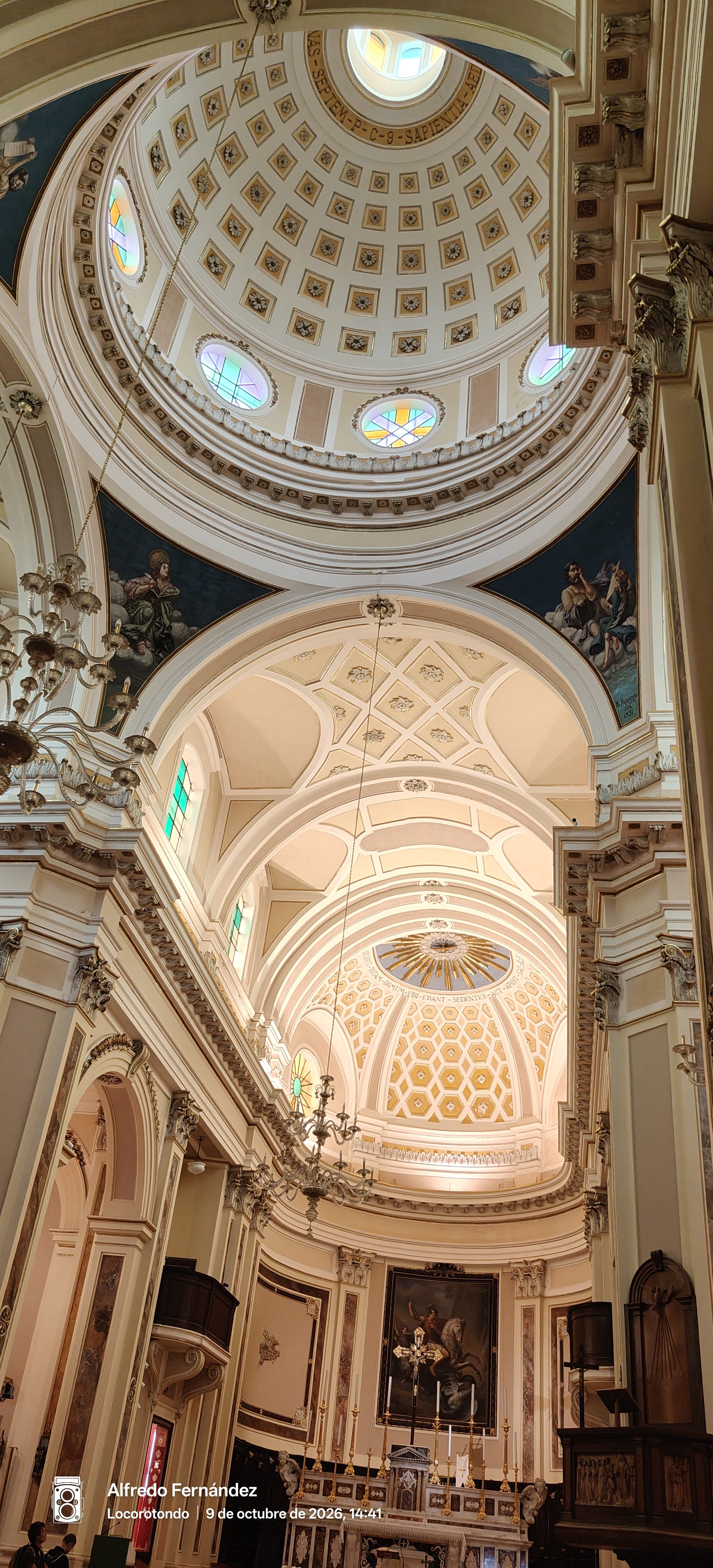 Interior de una iglesia luminosa con gran cúpula decorada, arcos ornamentados y altar al fondo.