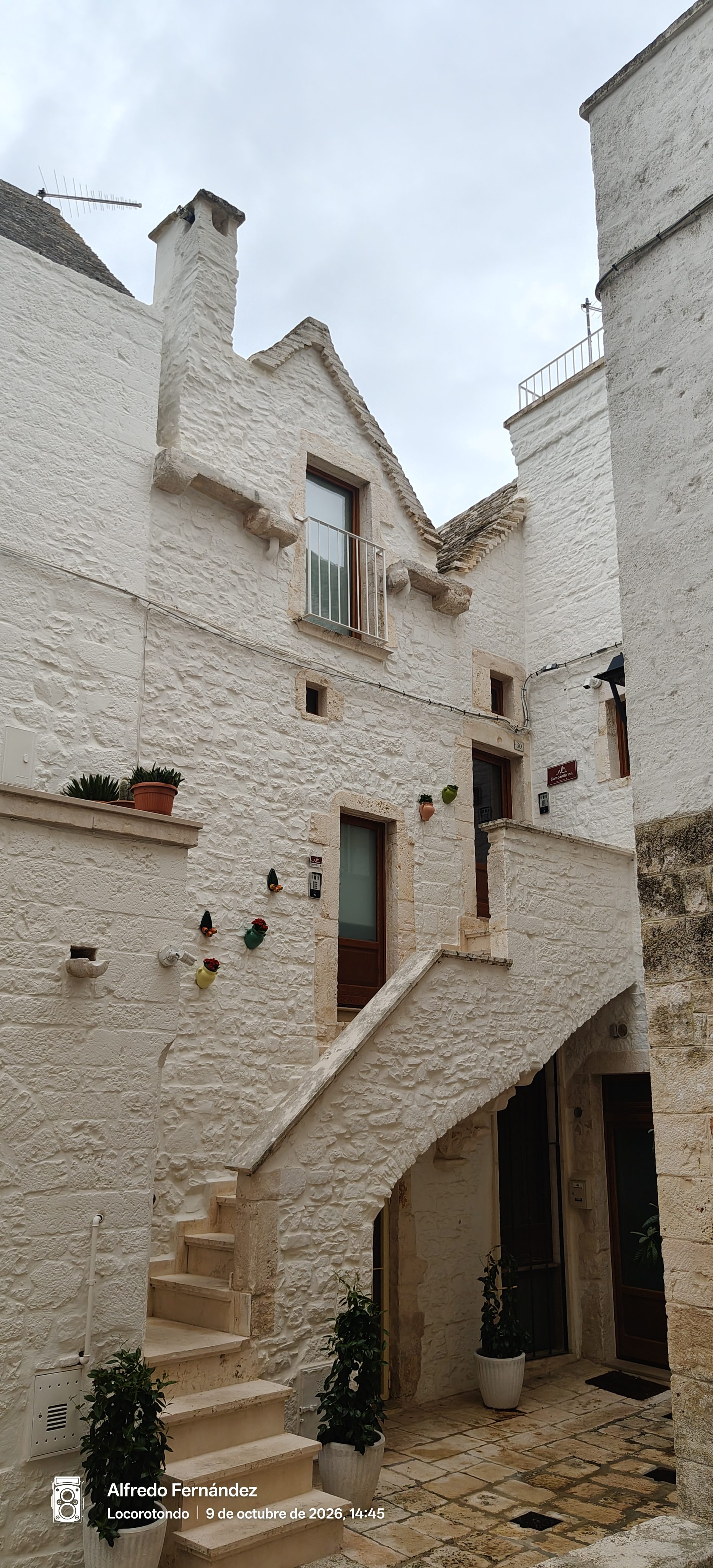 Fachada encalada tradicional con escalera de piedra exterior y macetas en Locorotondo.