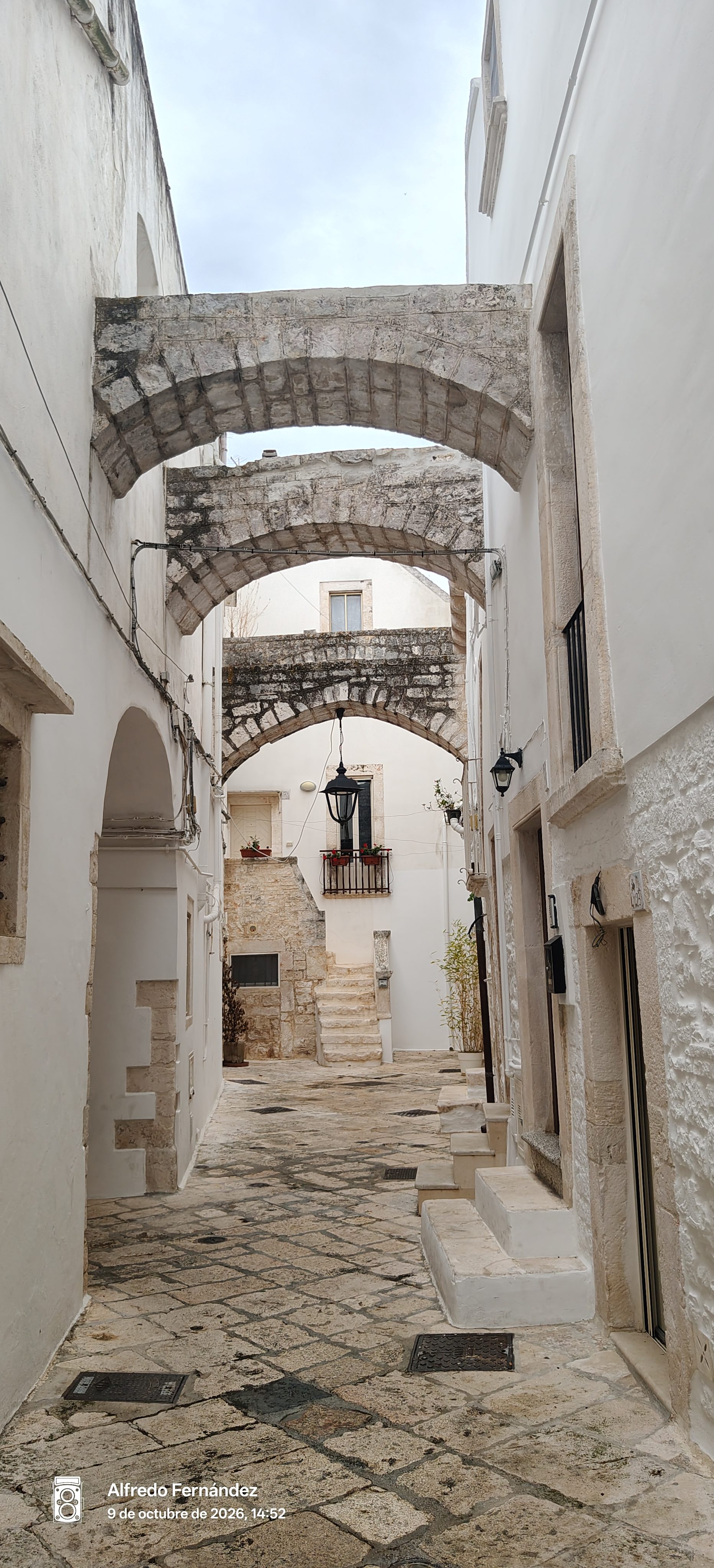 Callejuela empedrada con casas blancas y arcos de piedra en un pueblo antiguo.