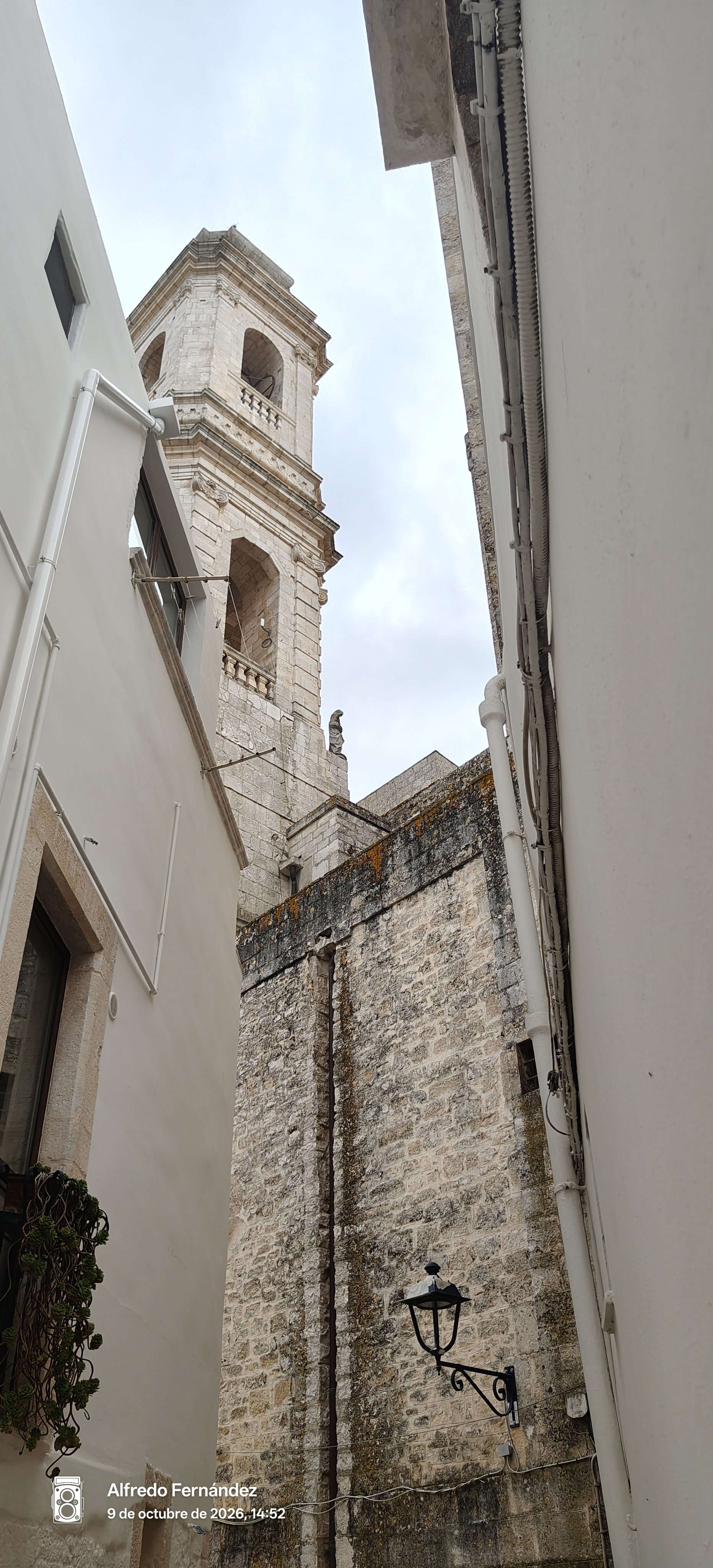 Campanario de piedra visto desde un callejón estrecho con paredes blancas en Locorotondo.