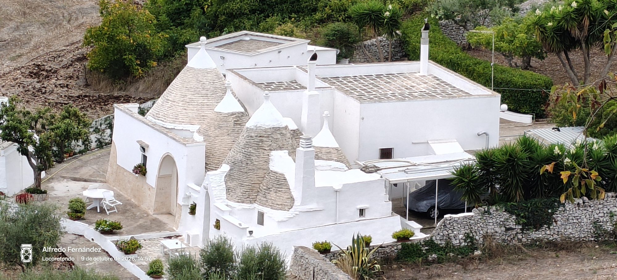 Casa tradicional con tejados cónicos tipo trullo y paredes blancas rodeada de vegetación.