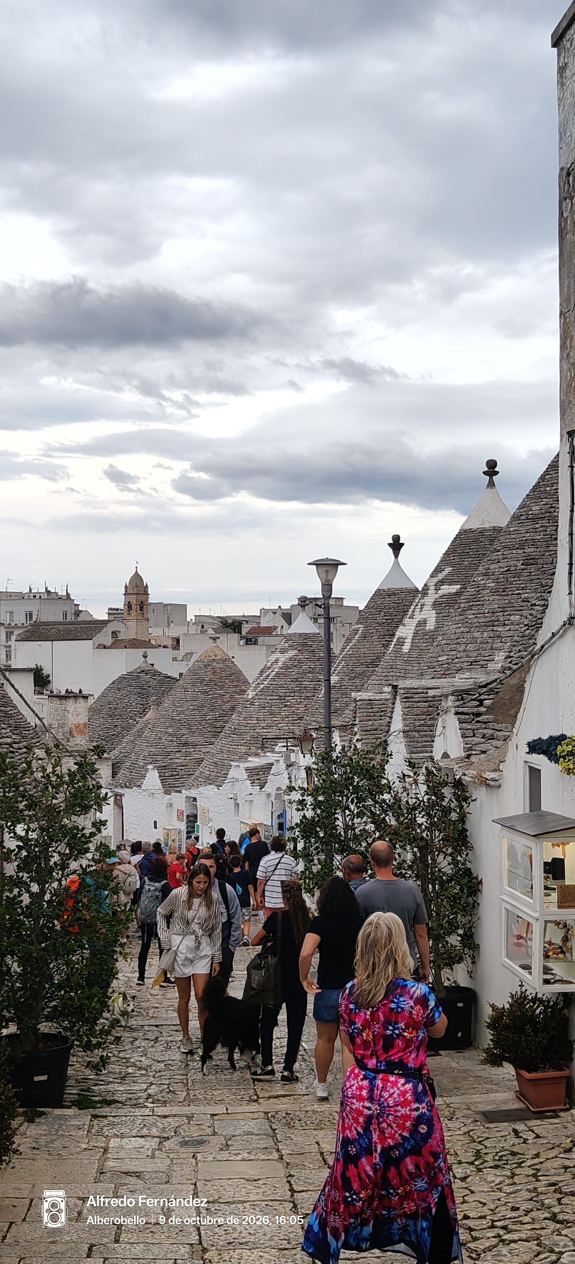 Calle empedrada con tradicionales trulli de techos cónicos en Alberobello con visitantes paseando.