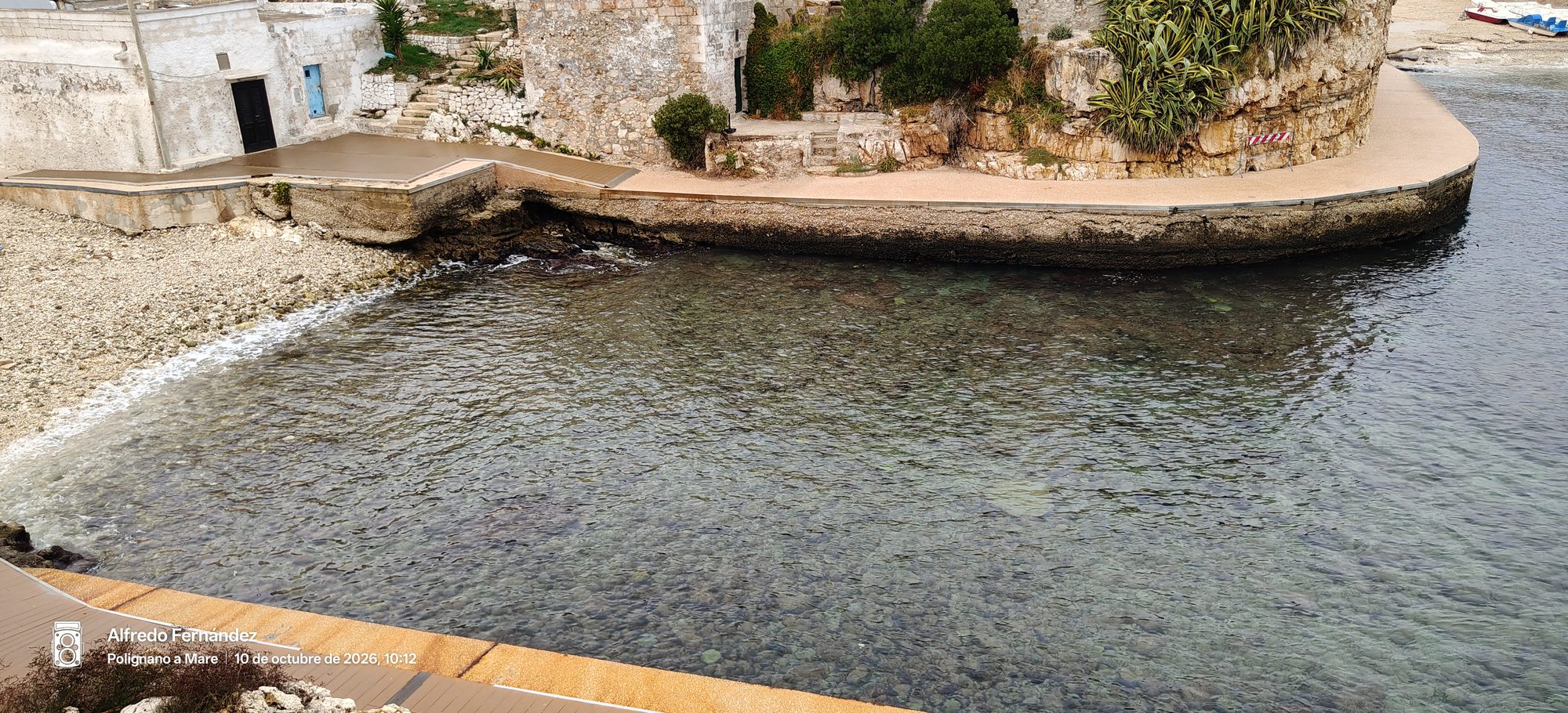 Cala de aguas cristalinas y fondo pedregoso flanqueada por muros de piedra tradicionales.