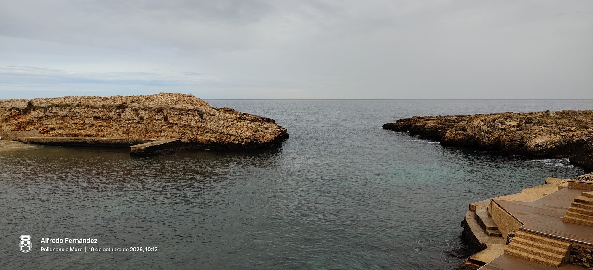 Entrada al mar entre acantilados rocosos y aguas tranquilas bajo un cielo nublado.