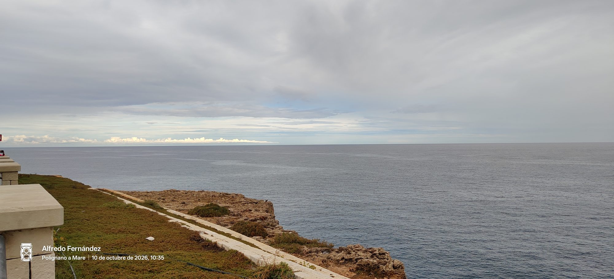 Acantilado rocoso con vistas al mar abierto bajo un cielo gris nublado.
