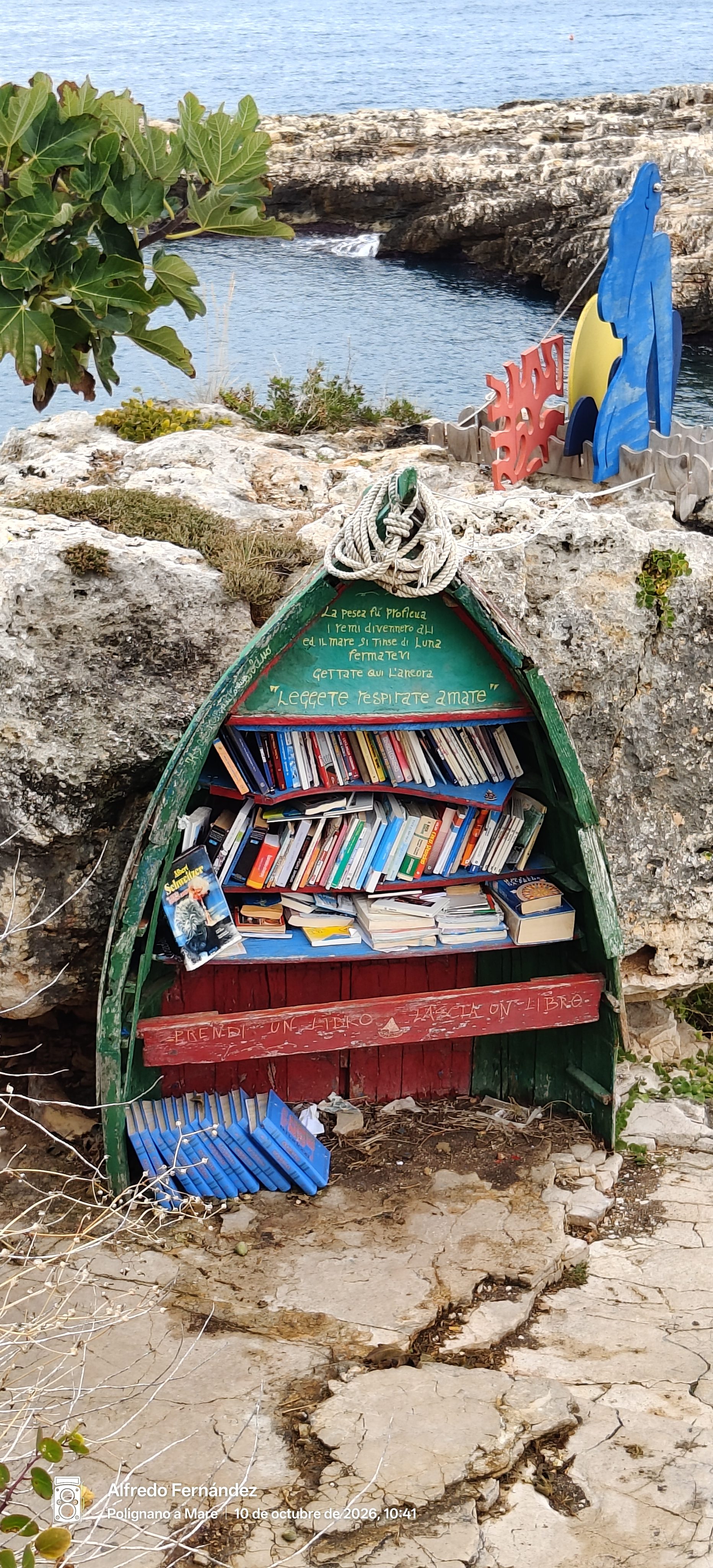 Barca tradicional convertida en estantería de libros sobre las rocas frente al mar.