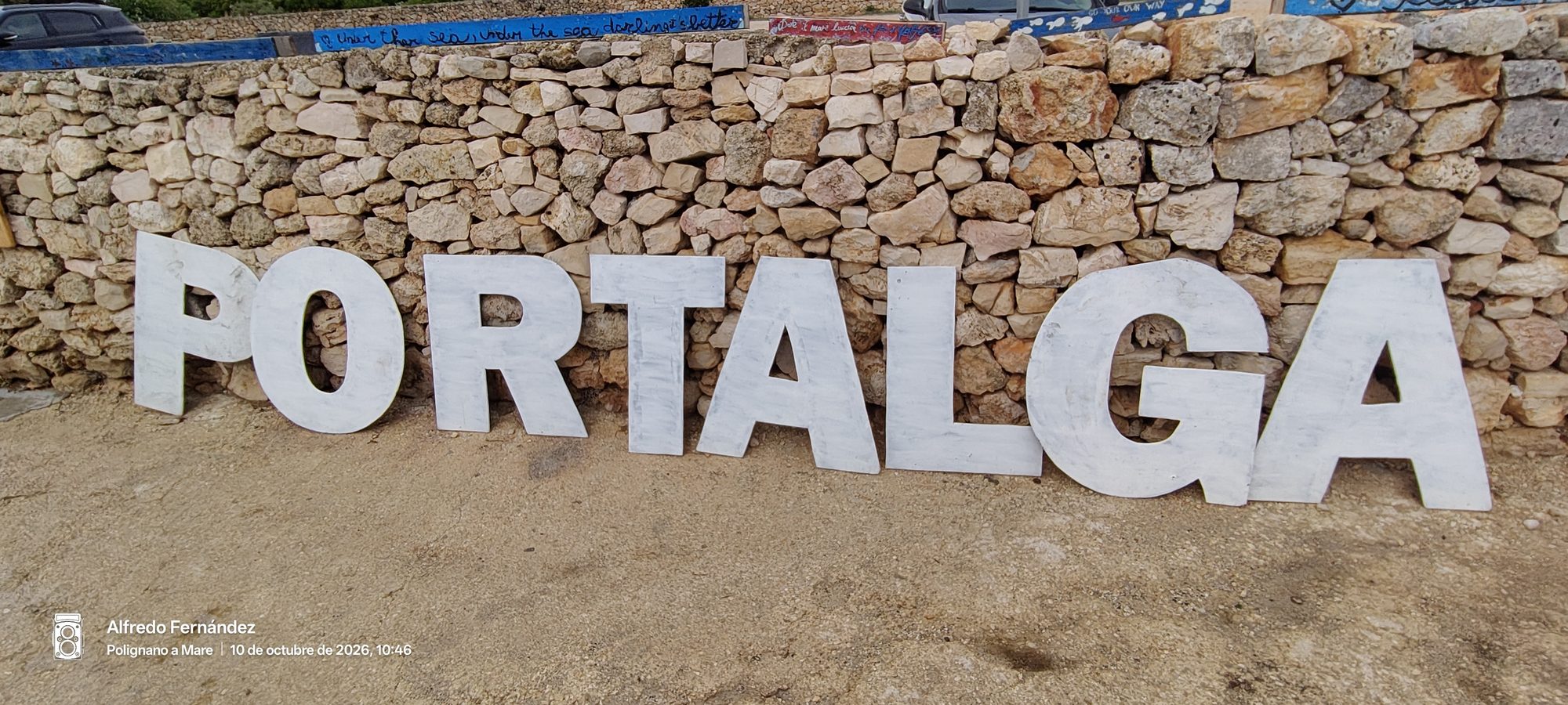 Letras blancas gigantes formando el nombre Portalga apoyadas sobre un muro de piedra rústico.