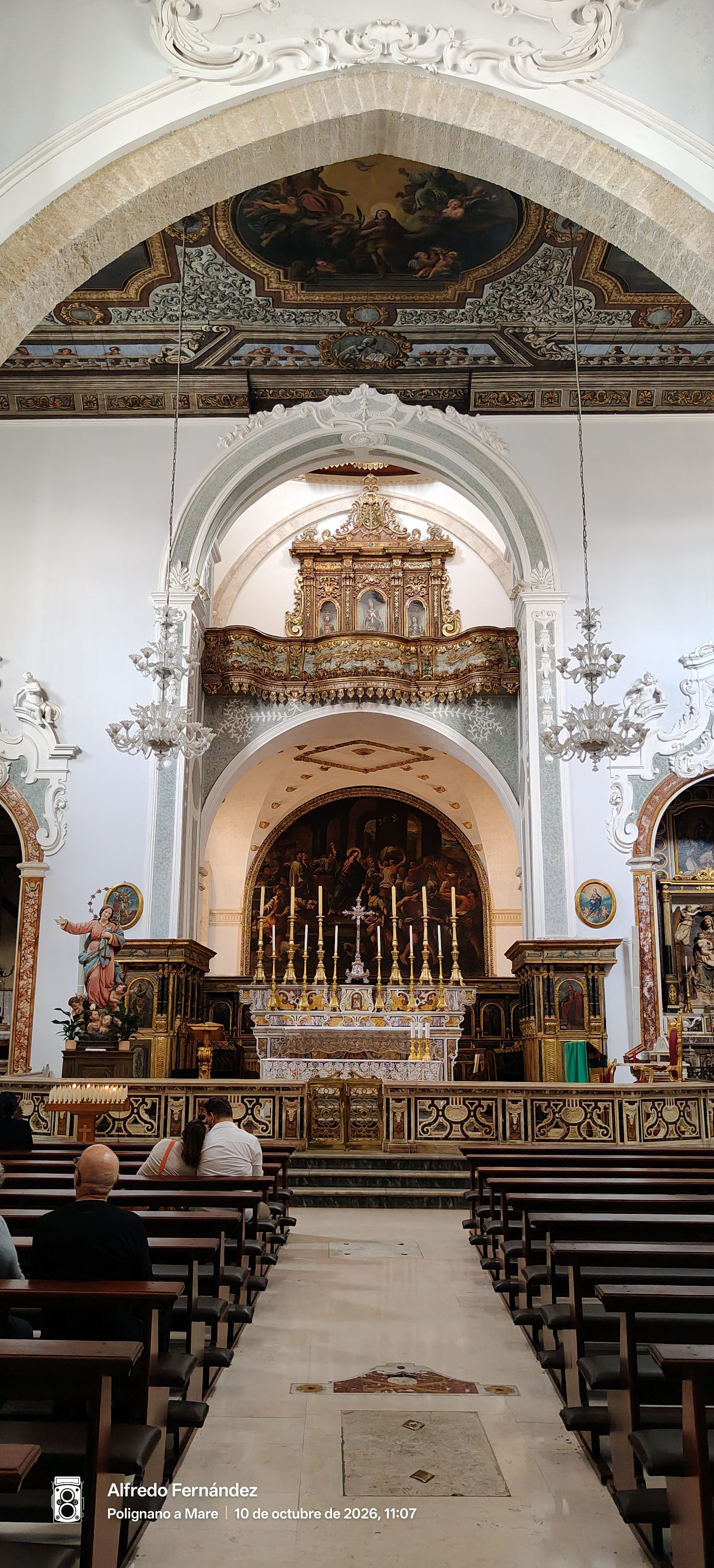 Altar mayor ornamentado y techo con frescos en una iglesia histórica con bancos de madera.
