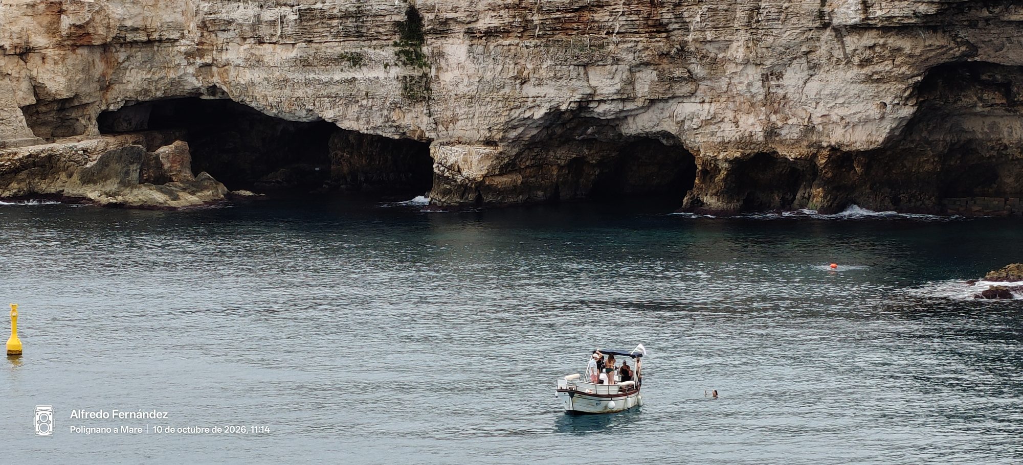 Pequeña barca navegando frente a cuevas y acantilados marinos de roca caliza.