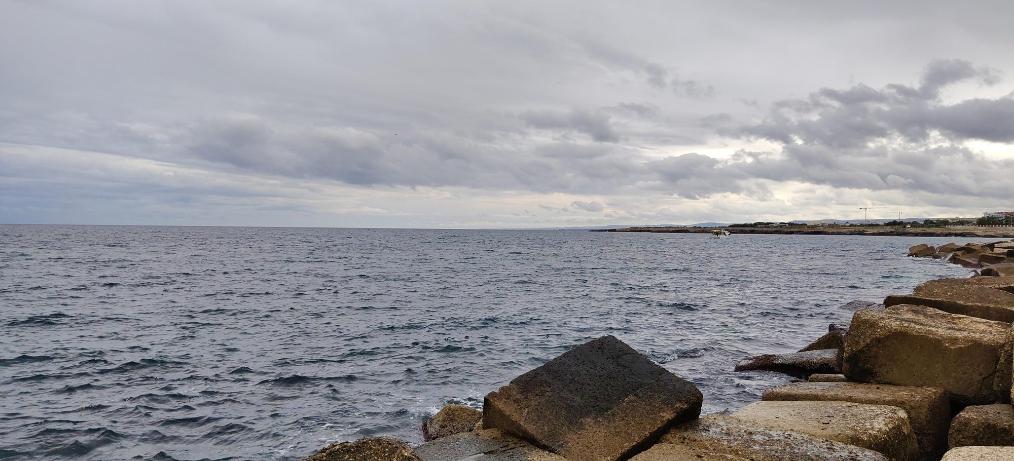Espigón de rocas frente al mar Adriático bajo un cielo cubierto de nubes.