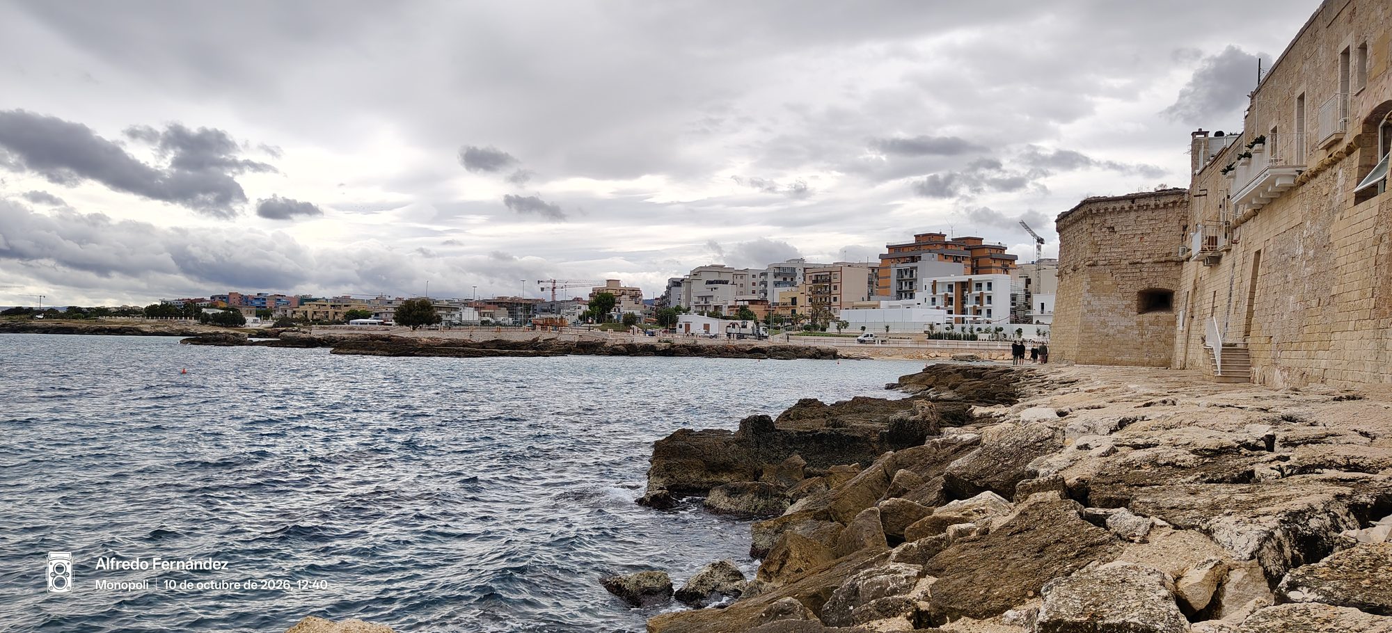 Muralla de piedra y orilla rocosa frente al mar en Monopoli bajo nubes grises.