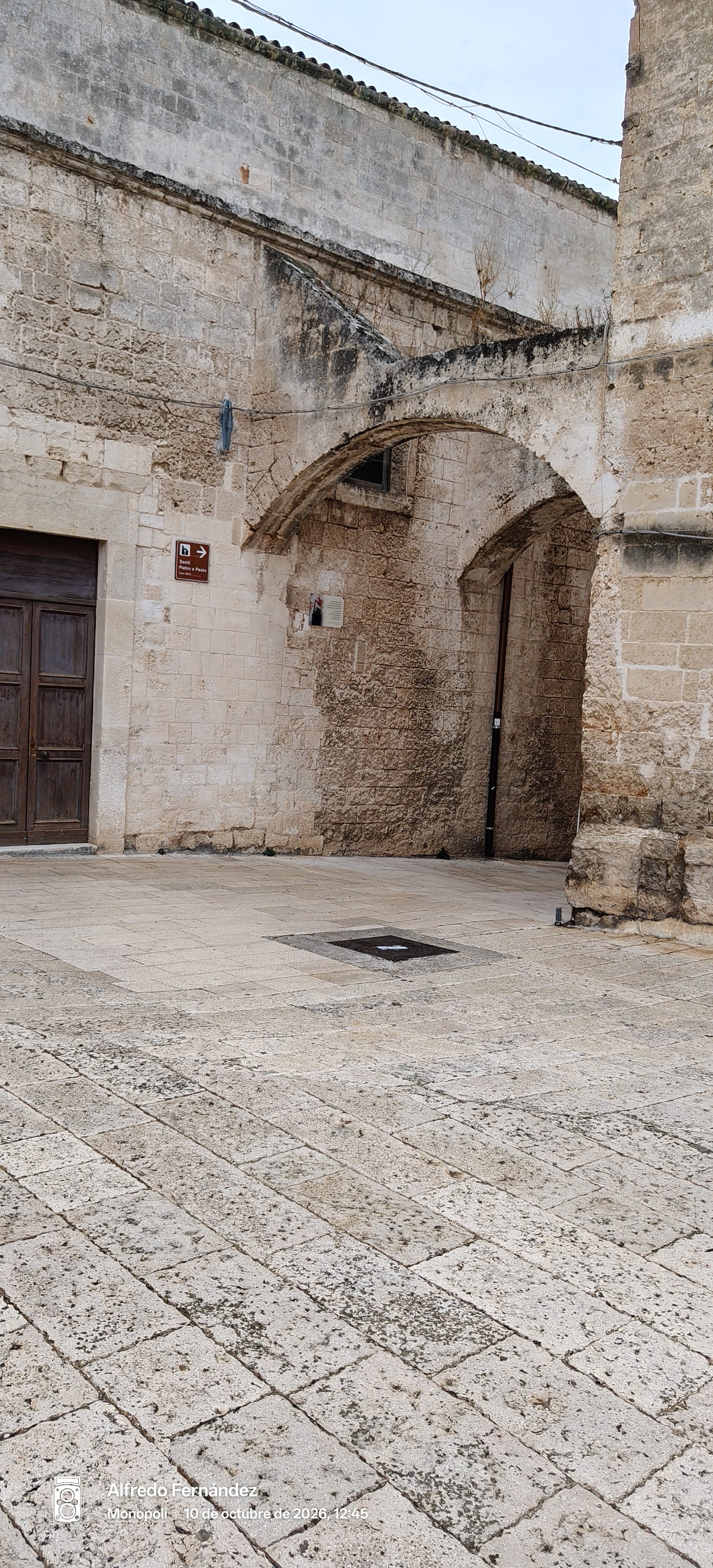 Plaza empedrada con antiguos arcos y muros de piedra caliza en un rincón histórico.