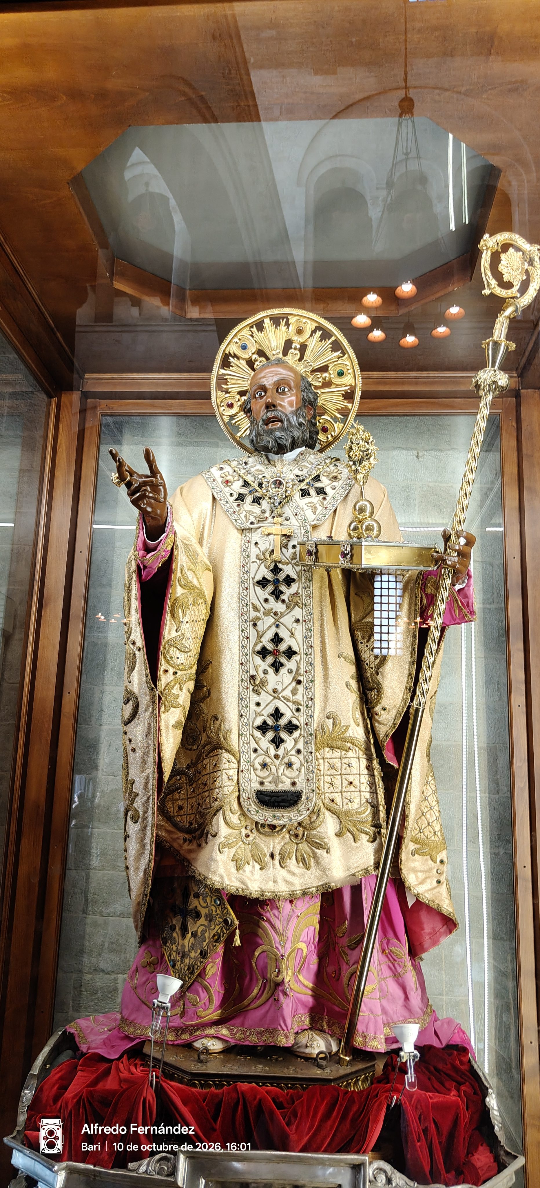 Estatua de San Nicolás con ornamentadas vestiduras doradas y báculo dentro de una vitrina.