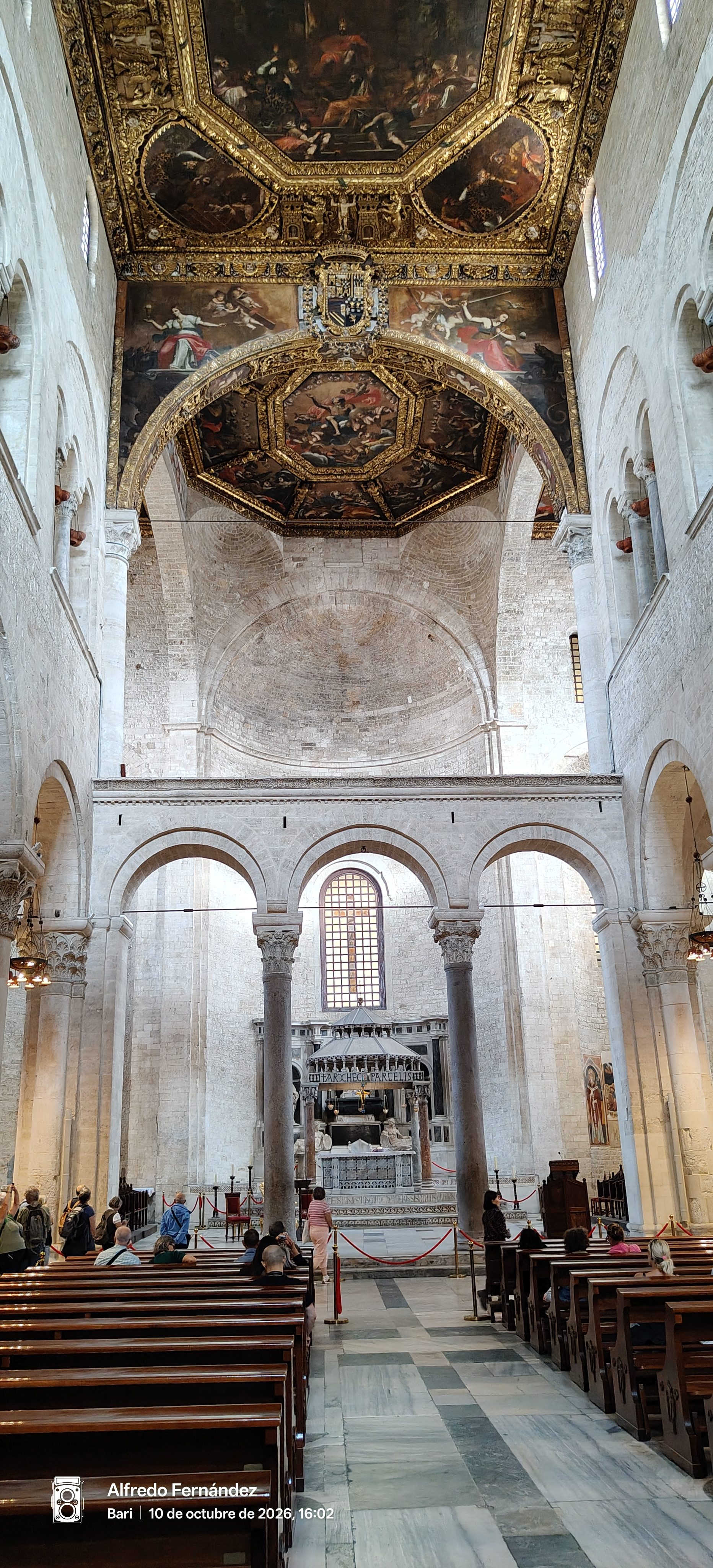 Interior de basílica de piedra con arcos, altar y techo dorado decorado con pinturas.
