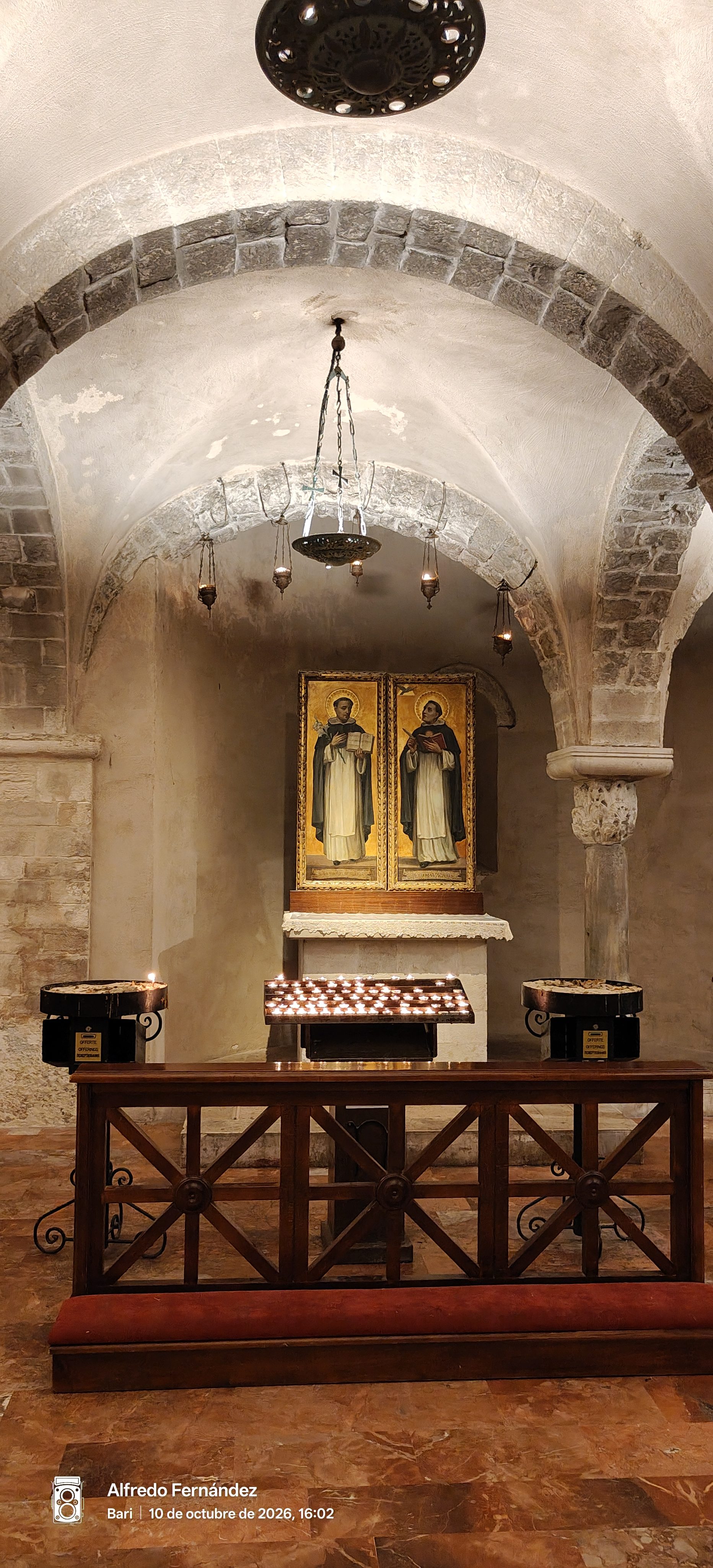 Capilla abovedada de piedra con velas encendidas, iconos religiosos y reclinatorio de madera.