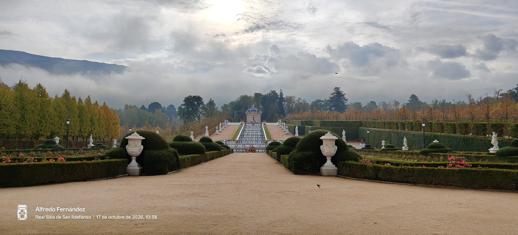 Jardines clásicos con setos podados, jarrones de piedra y montañas envueltas en niebla.