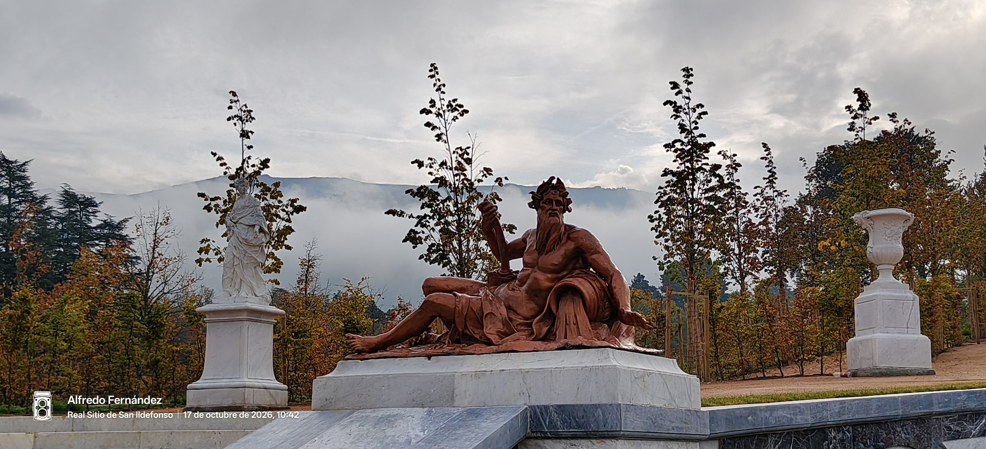 Estatua clásica reclinada en los jardines de La Granja con montañas entre la niebla.